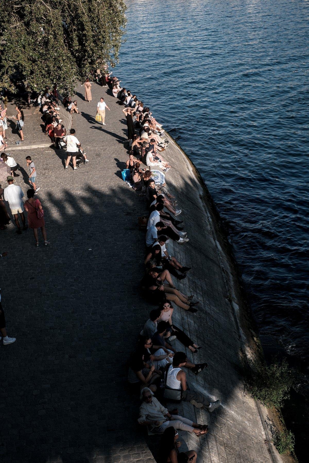Photo verticale. Vue de dessus des quais de la Seine où plein de gens sont installé en bord de quai pour observer l’éclipse
