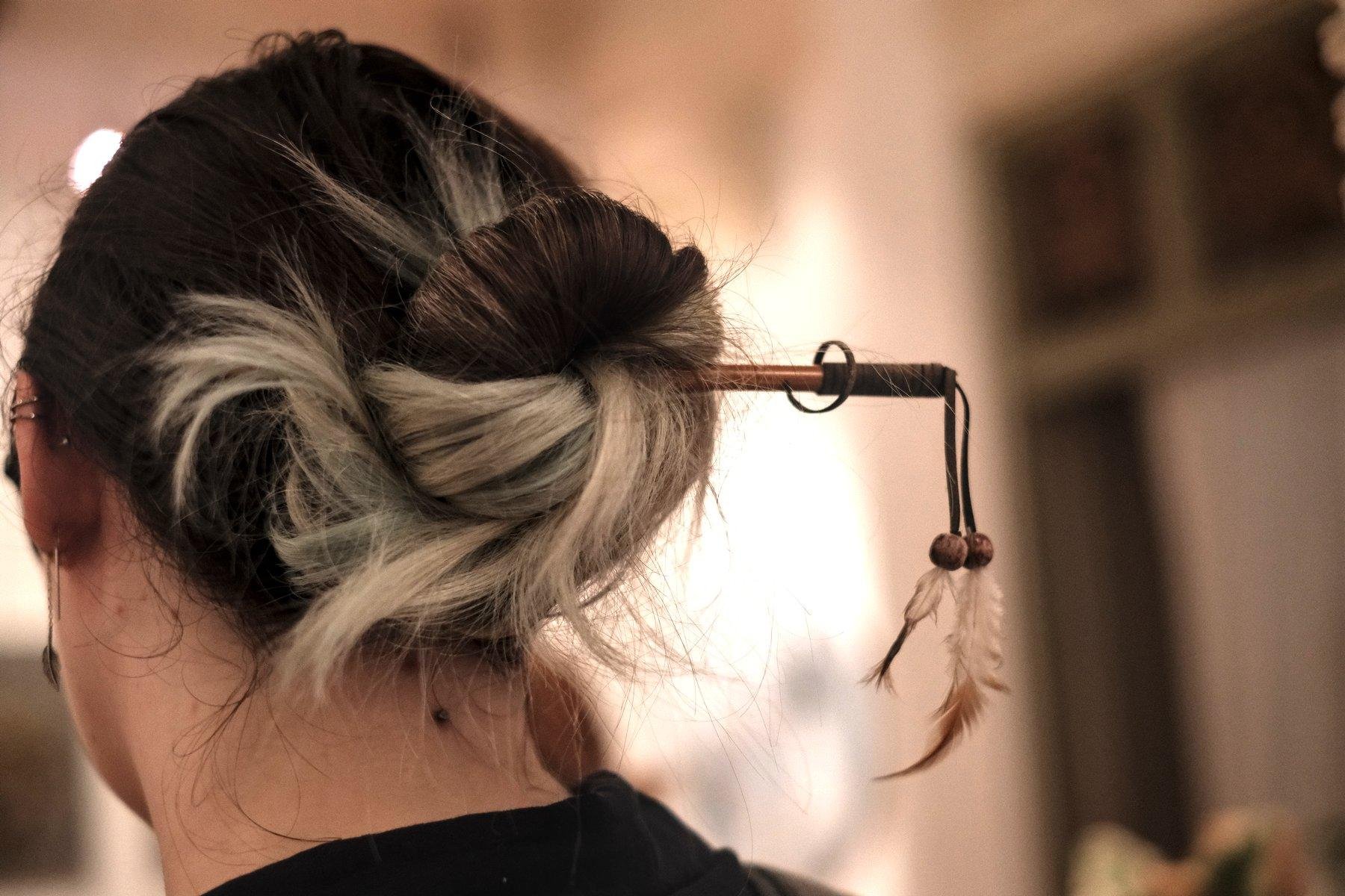 Photo horizontale. Gros plan sur une baguette décorée servant à tenir un chignon de cheveux bruns, bleu et blanc.