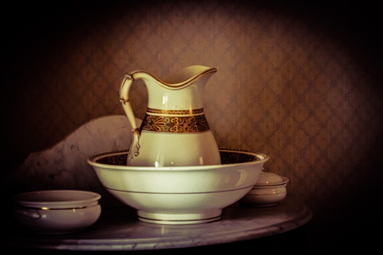 The image shows a vintage-style ceramic pitcher and basin set, often used in past centuries for washing. The set features decorative patterns, possibly in a classic or Victorian style, and is placed on a surface, suggesting a historical or antique setting.