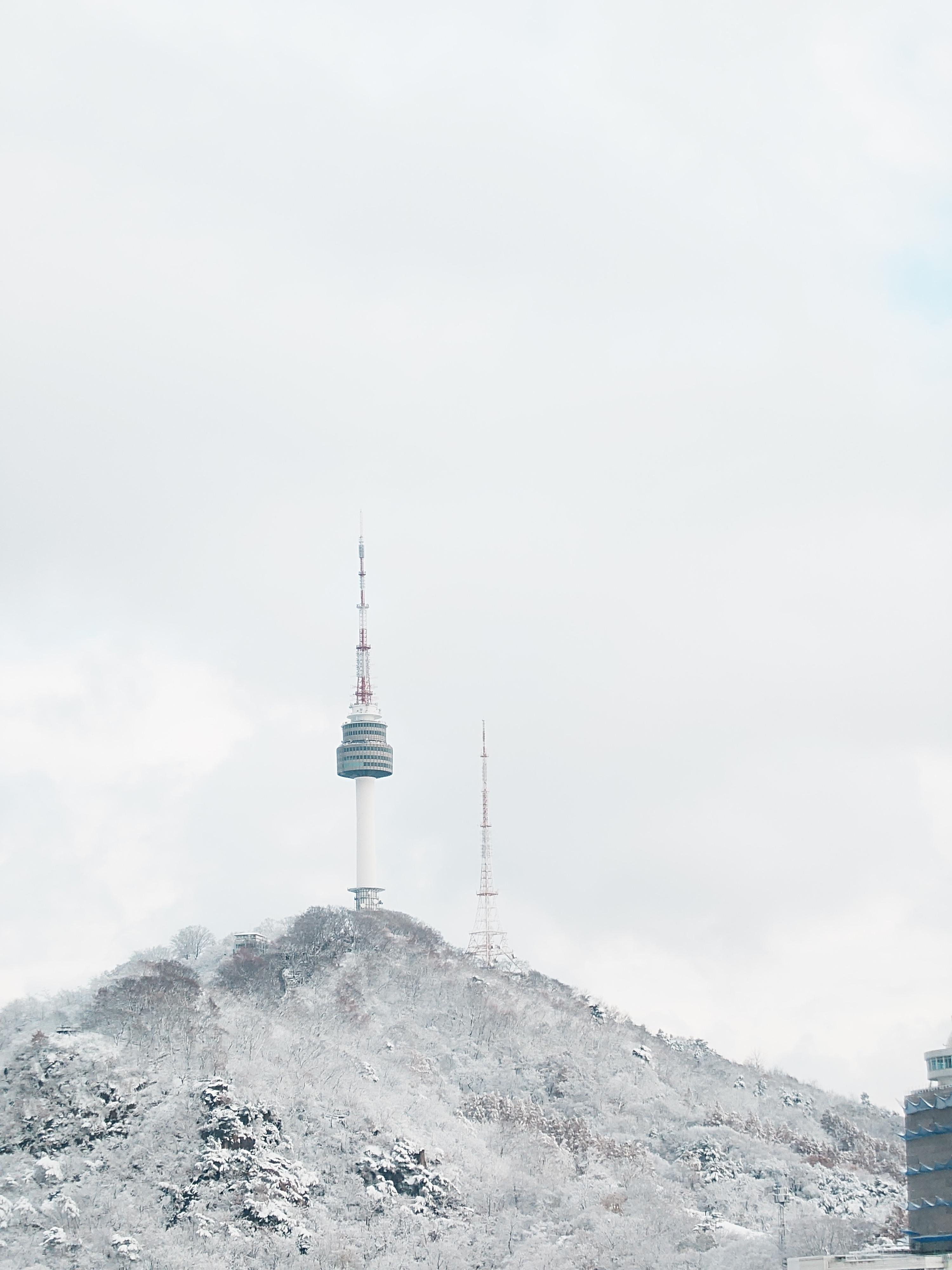 The image shows a snowy landscape with a prominent tower, likely a communication or observation tower, on a hill. The sky is overcast, and there is a second smaller antenna nearby. The scene gives a cold, wintery feel.