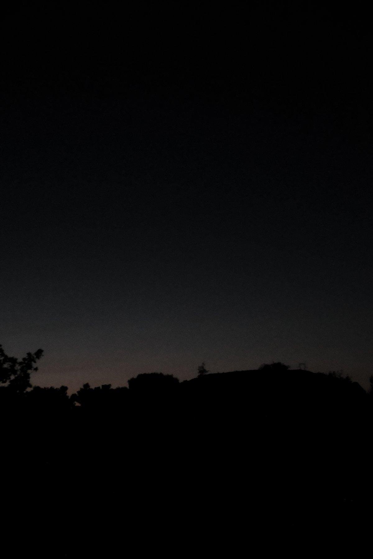 Photo verticale. Un dégradé de ciel du violet nuit sombre au rose du soleil couchant derrière une chaîne de montagne se dessinant en contre jour, puis le noir