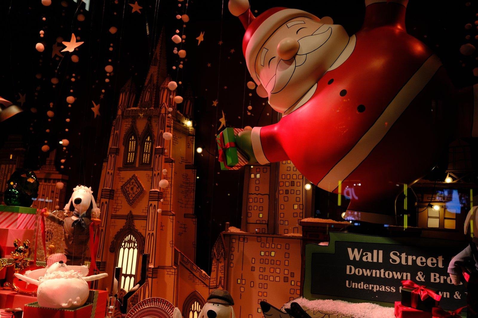 Photo d’une vitrine décorée sur le thème de Wall Street à Noël, avec plein de figurines de chiens anthropomorphes et un père noël géant pendu au plafond de la vitrine