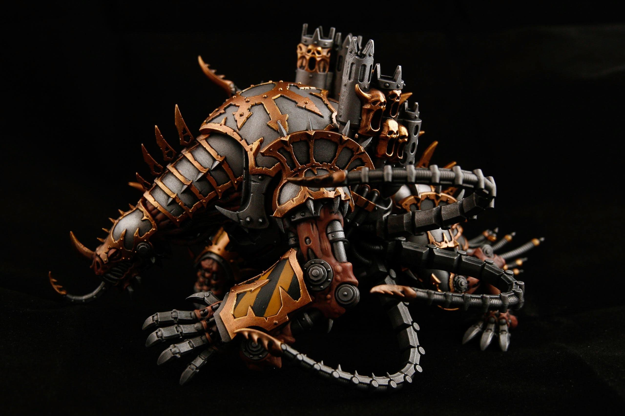 The image shows a detailed miniature model of a creature or machine. It appears to be a fantasy or science fiction figure, featuring metallic armor, spikes, and mechanical elements that resemble claws and limbs. The model has a dark color scheme with bronze and black accents. It looks intricate and may be used in tabletop gaming or as a collectible.