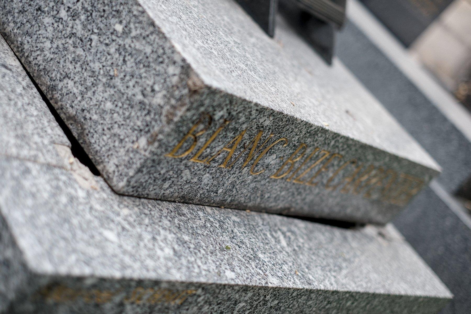 Photo horizontale. Cadrage en déséquilibre, gros plan sur une tombe dont la pierre de couvercle n’est pas alignée, laissant des coins ouverts sur l’intérieur