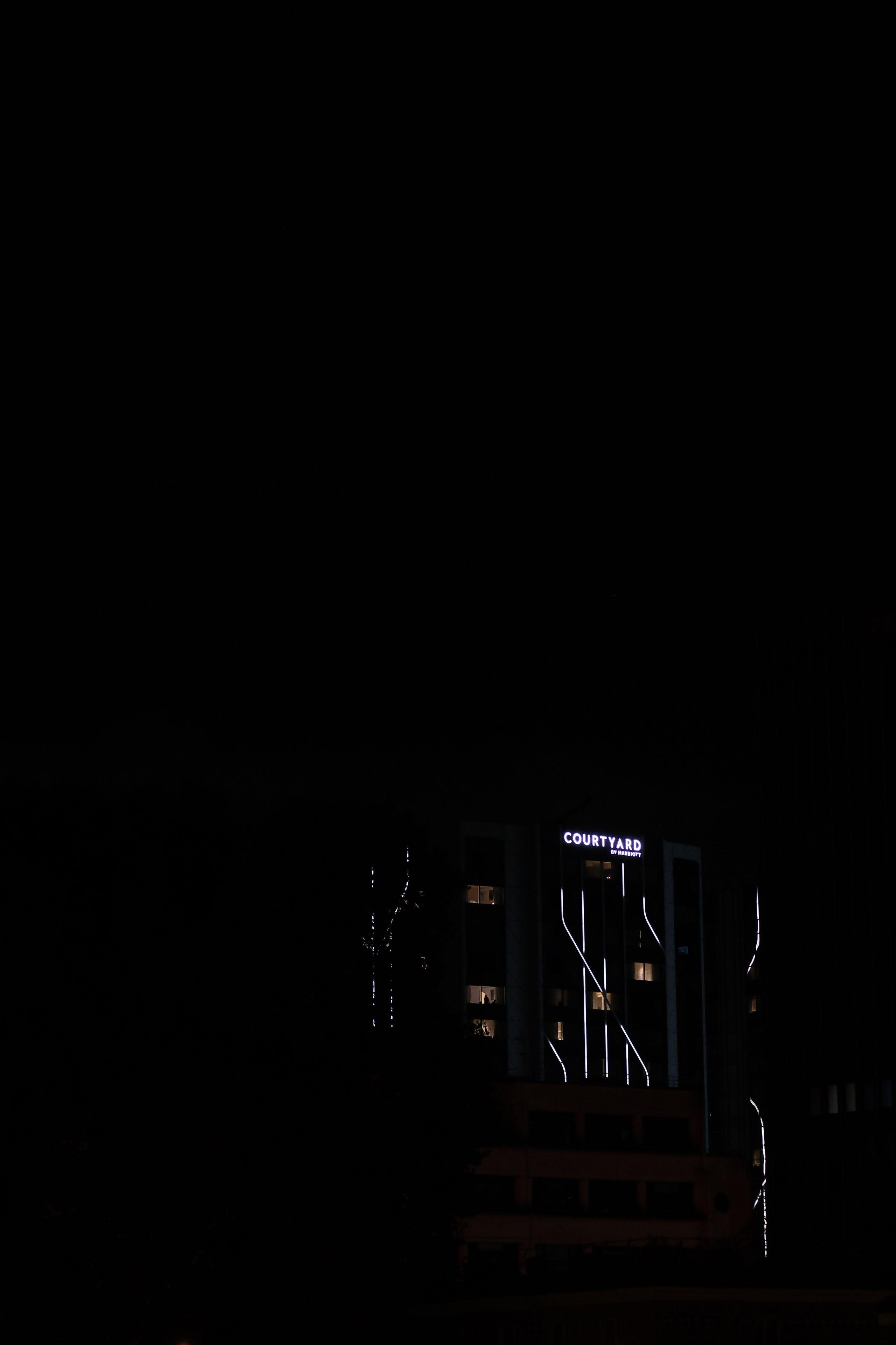 Photo verticale de nuit. On y voit dans le coin SE, des lignes de lumières sous une enseigne en lettres lumineuses «&nbsp;Courtyard&nbsp;»