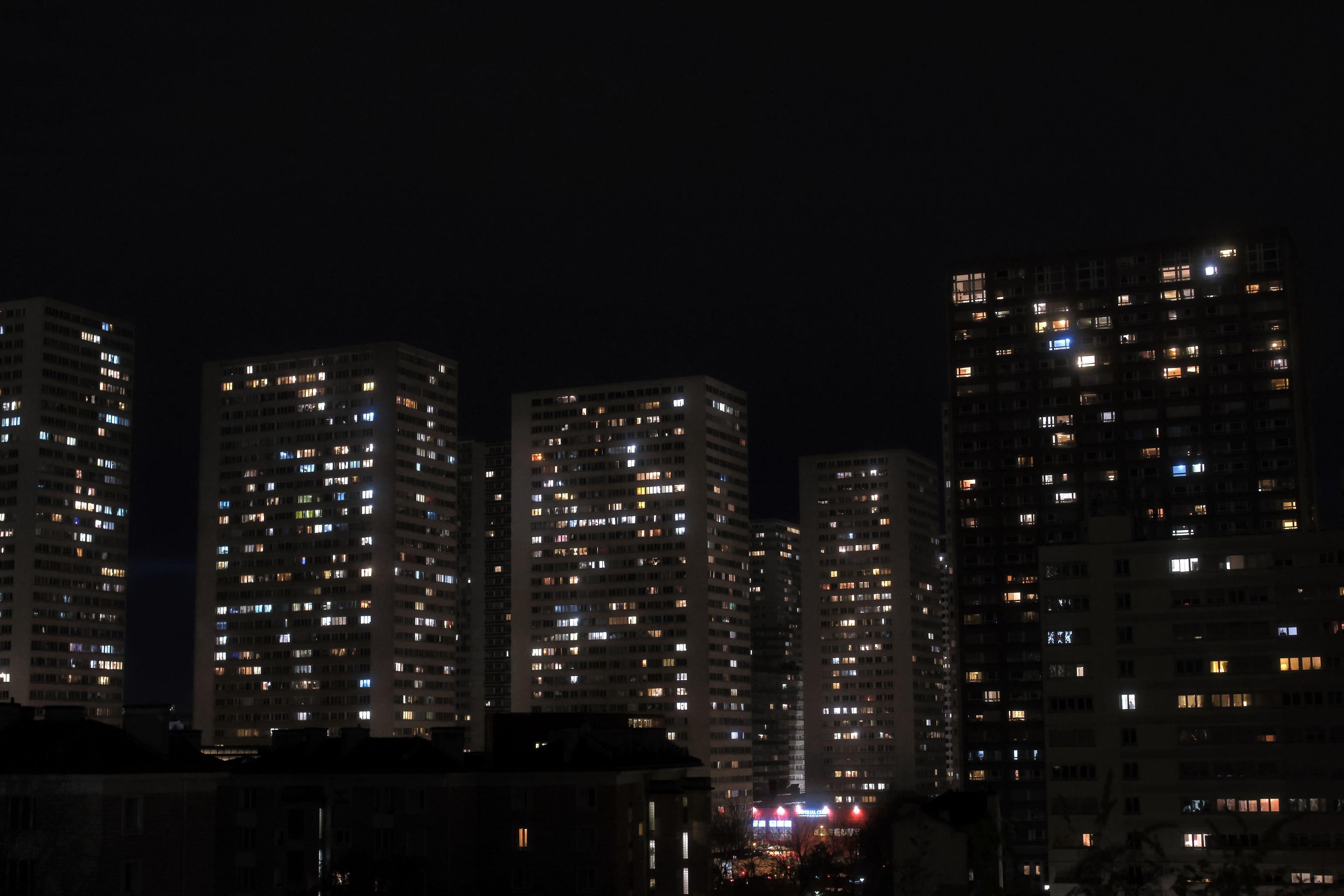 Photo format paysage, de nuit, montrant une vue dégagée sur les tours d’immeubles du 13e arrondissement de Paris, avec des fenêtres éclairées et d’autres non.