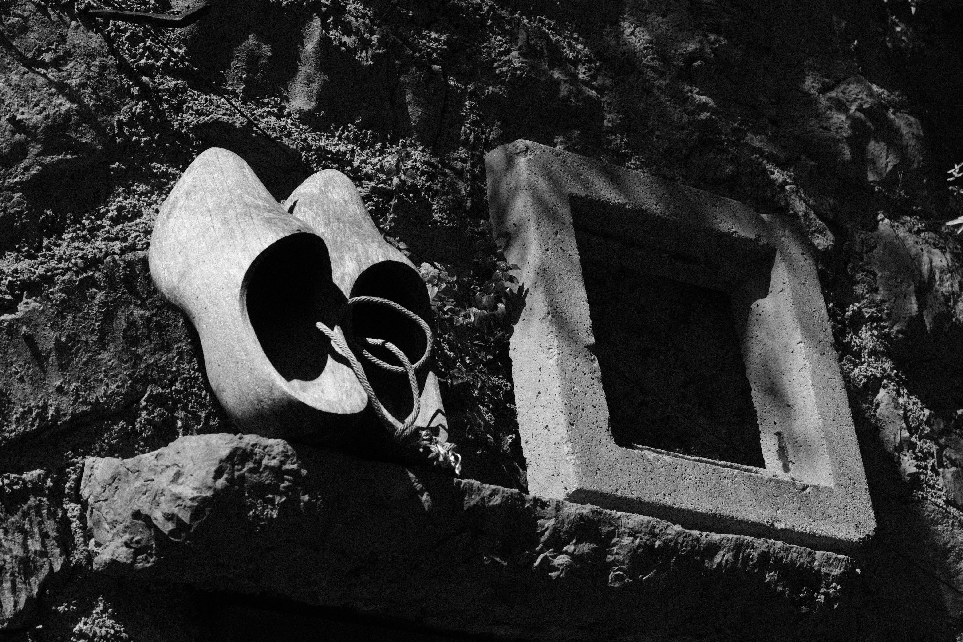 Wooden shoes and an empty rectangular frame sitting on a shelf on a rough stone wall. Shot from slightly below.