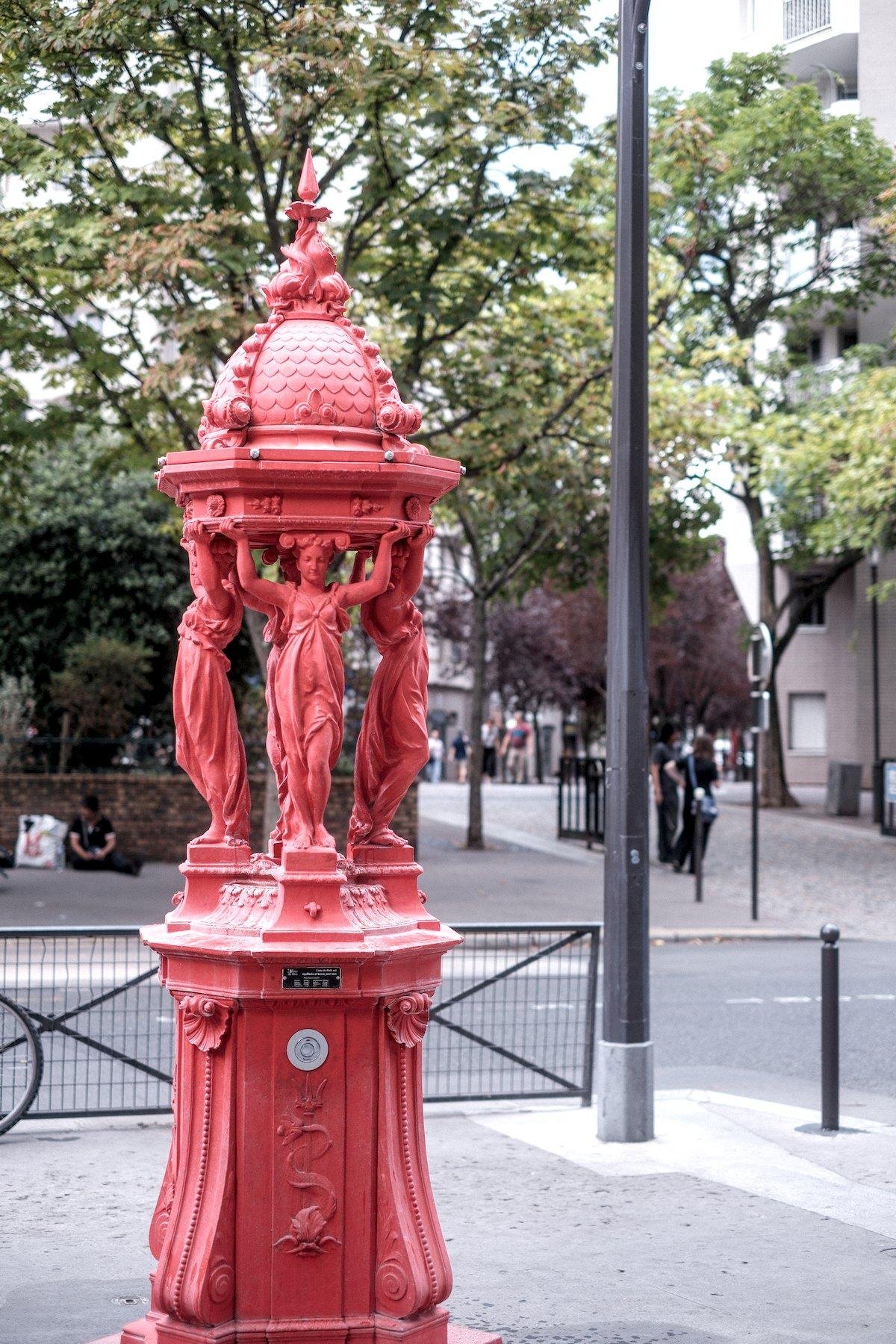 Photo verticale. Une fontaine parisienne, d’habitude verte, est rouge ici