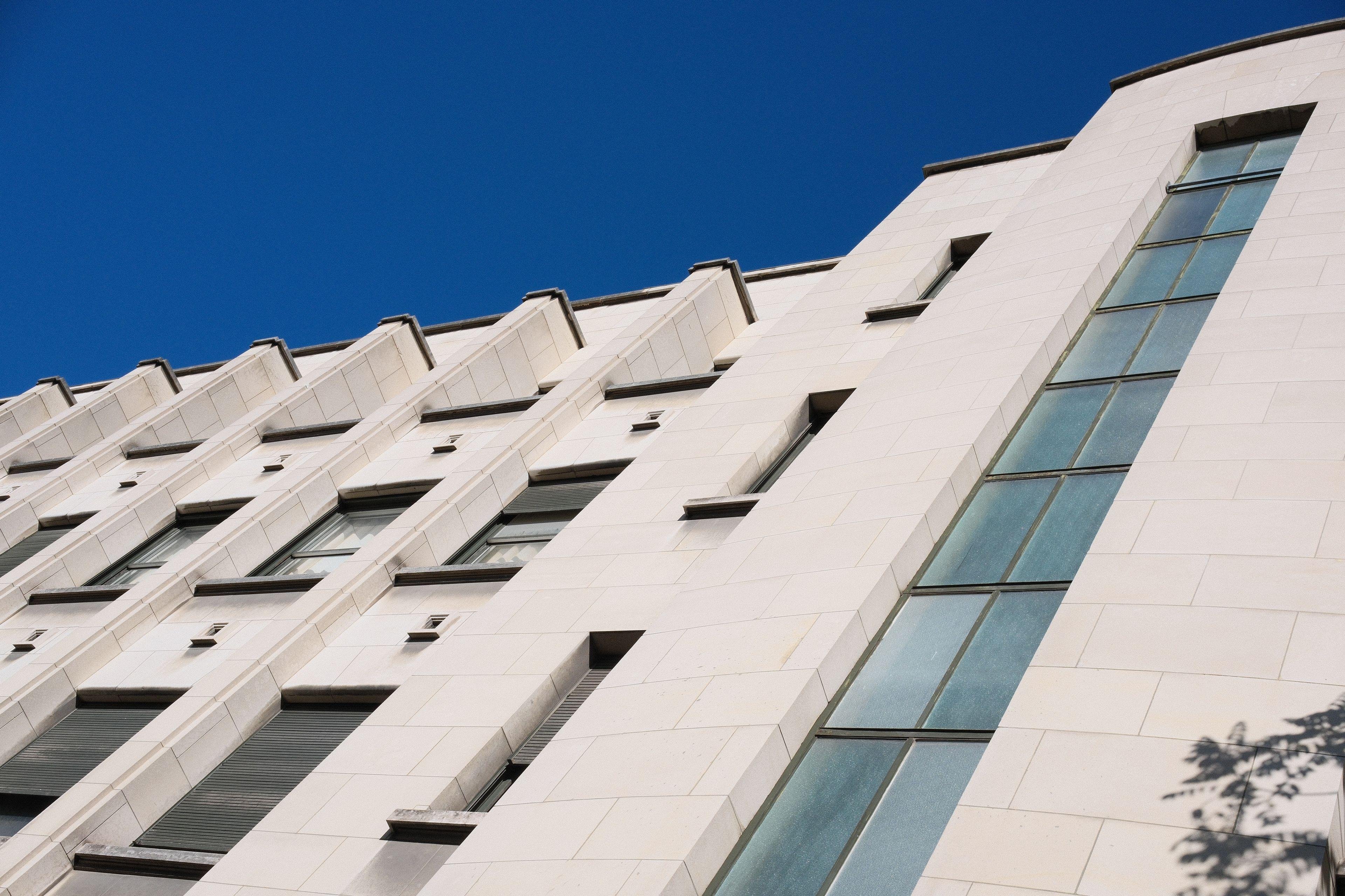 Contre plongée sur une Façade blanche d’un vieux bâtiment, ensoleillée, avec un ciel bleu pur derrière