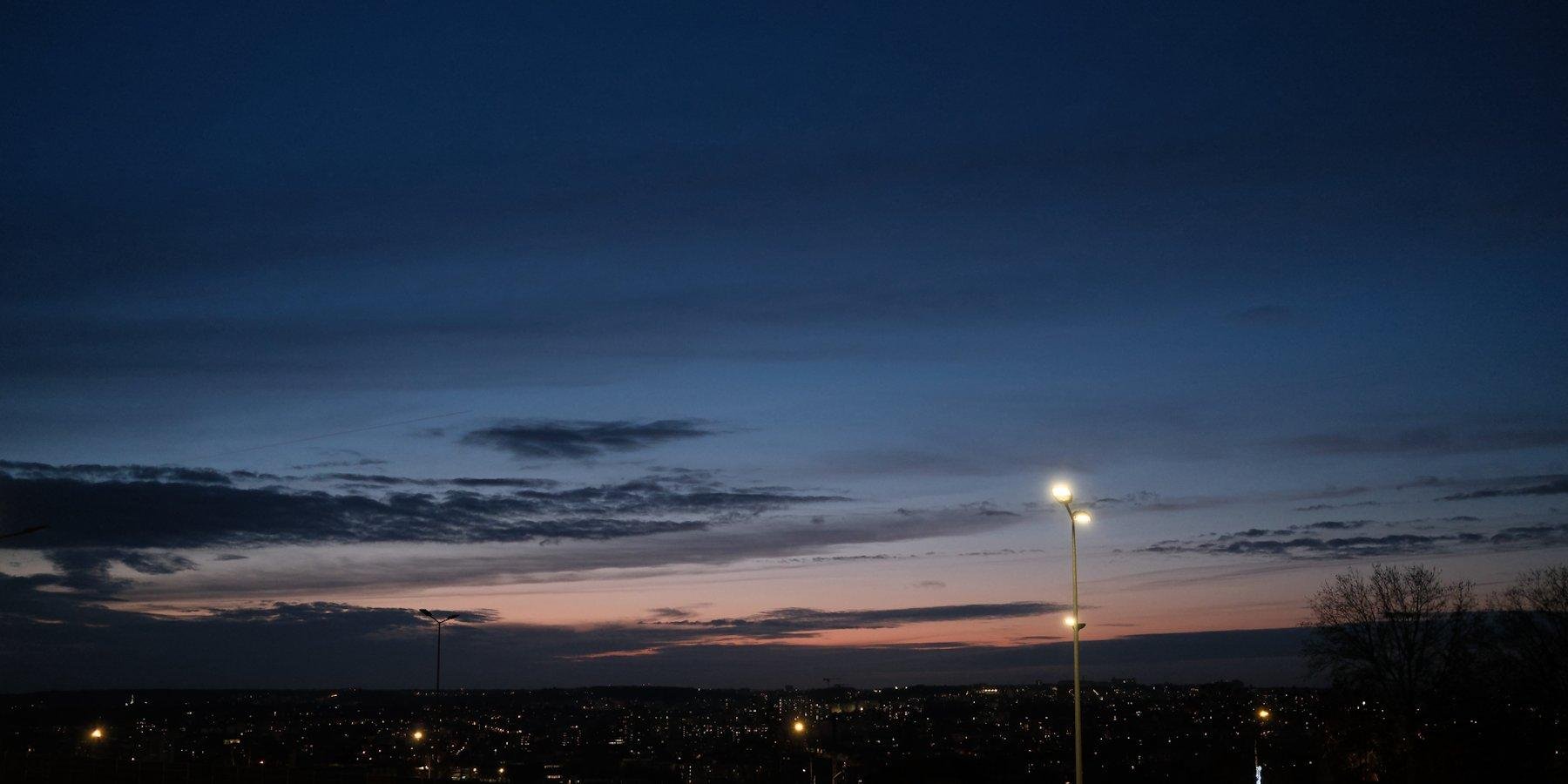 Photo horizontale. Ciel de crépuscule, avec ses teintes de bleu et rose. Des lumières de lampadaires sont visible en bas de l’image