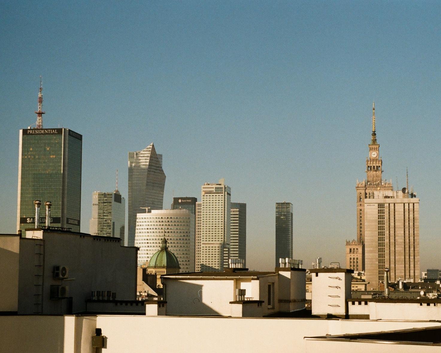 The image shows a cityscape featuring modern skyscrapers and historical architecture. The skyline includes various tall buildings, one of which appears to have a dome, indicating a blend of architectural styles. The overall setting suggests an urban area with diverse structures.