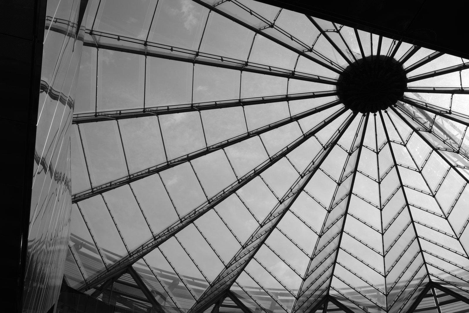 Photo format paysage en noir et blanc, montrant une structure circulaire avec son centre cadré en haut à droite, et des rayons qui en partent dans toutes les directions