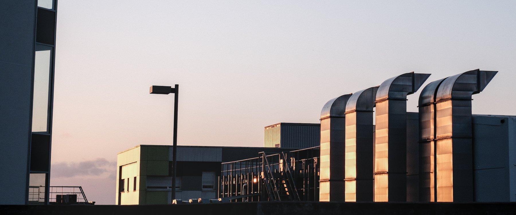 Photo horizontale ratio anamorphique. La lumière du soleil couchant sur des tuyaux en métal, un bout de bâtiment, une passerelle extérieure et son escalier en métal