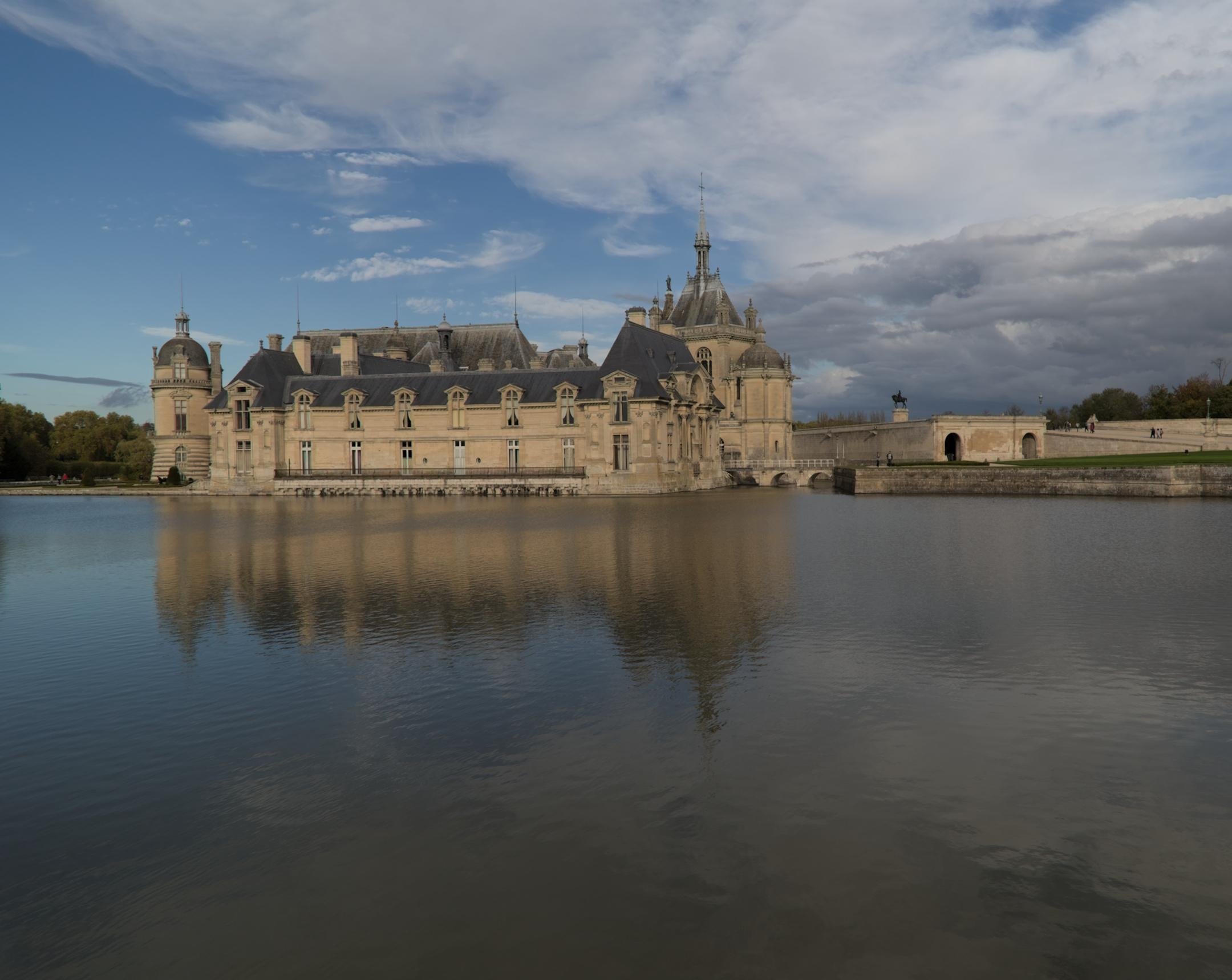 Le Château de Chantilly, se réfléchissant dans l’eau, le ciel est bleu avec des nuages