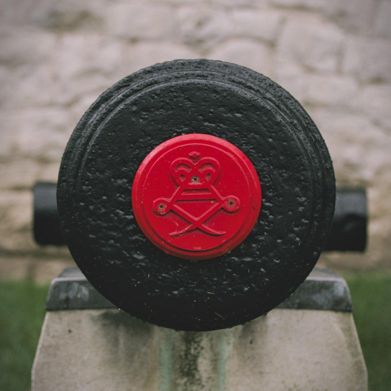 Photo carrée avec la bouche d’un canon noir de face, bouche scellée par un bouchon rouge avec un sceau de la Royal Artillery en relief dessus