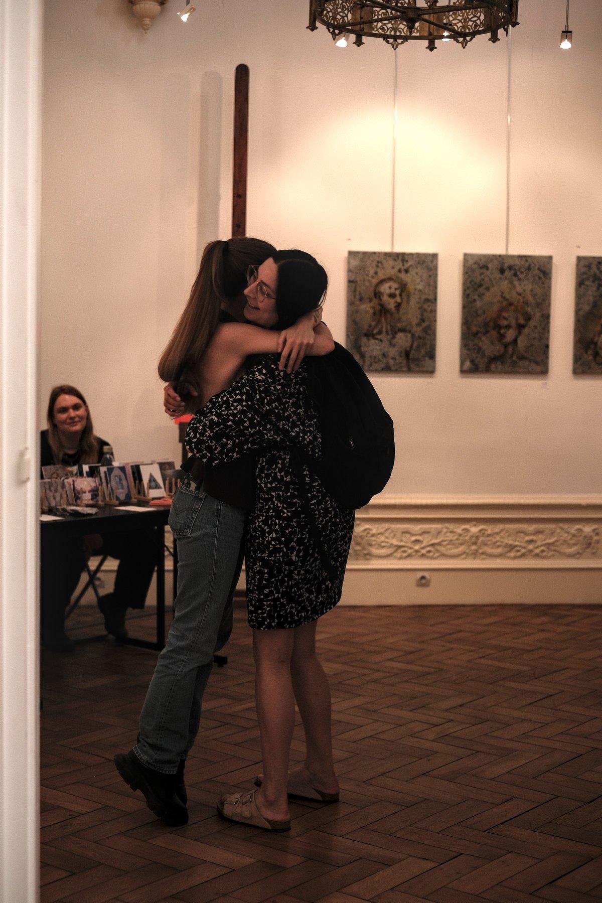 Photo verticale. Deux jeunes femmes sont enlacées lors de joyeuses retrouvailles dans une galerie d’art