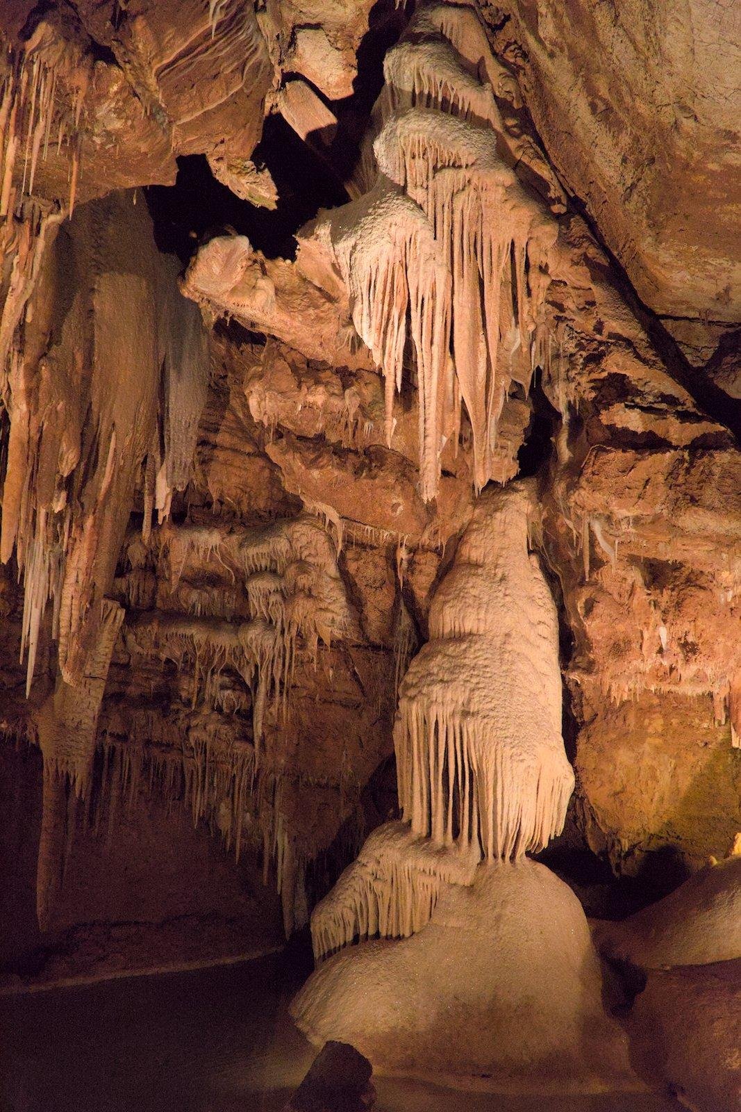Photo verticale. Sous terre, des concrétions de minerais sculptés par des millénaires de goutte à goutte pendant du «&nbsp;plafond&nbsp;»