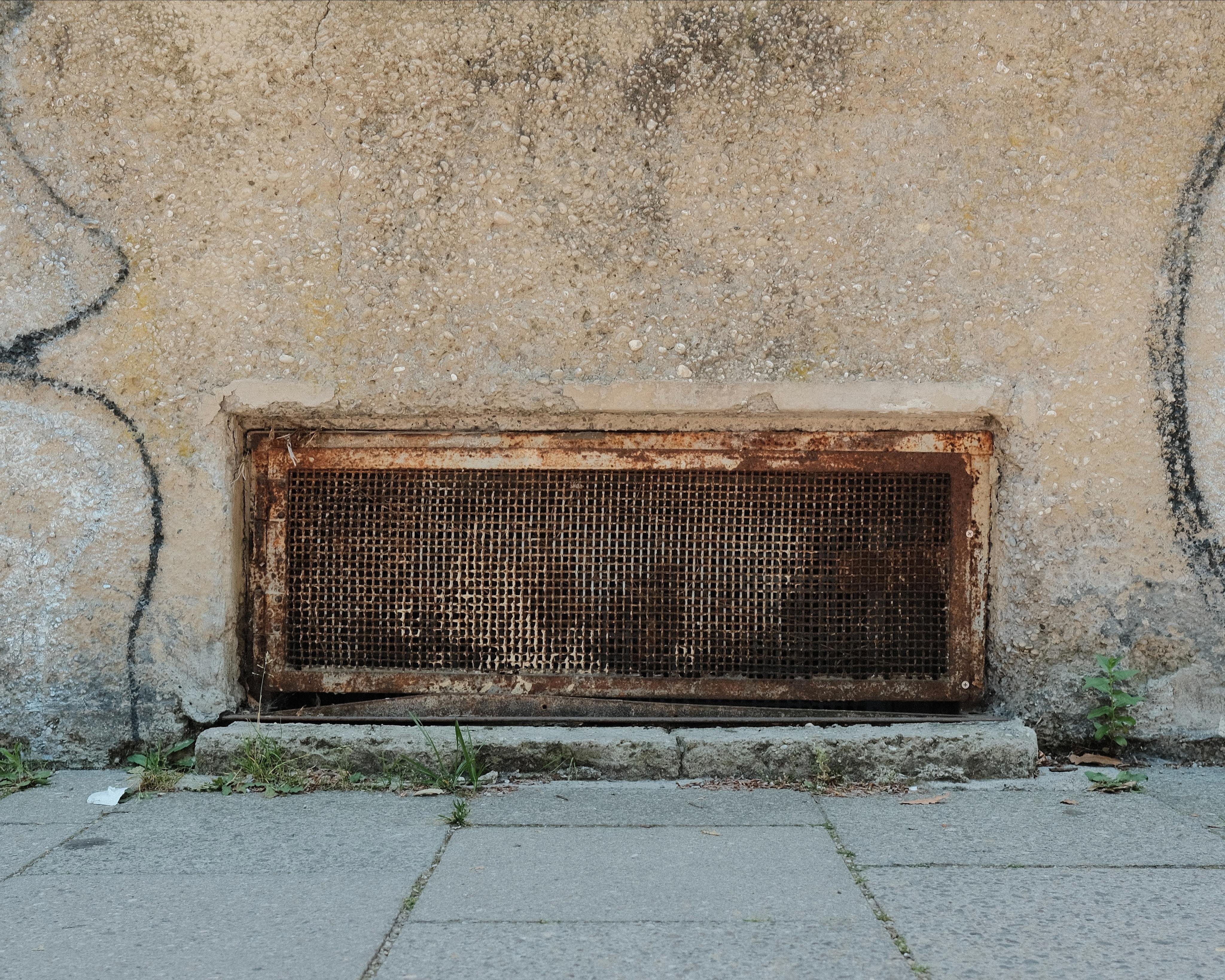 A smash window to a basement, sitting right on the level where facade and sidewalk meet. In front of the glass there is a dense rusty mesh preventing views into the cellar.