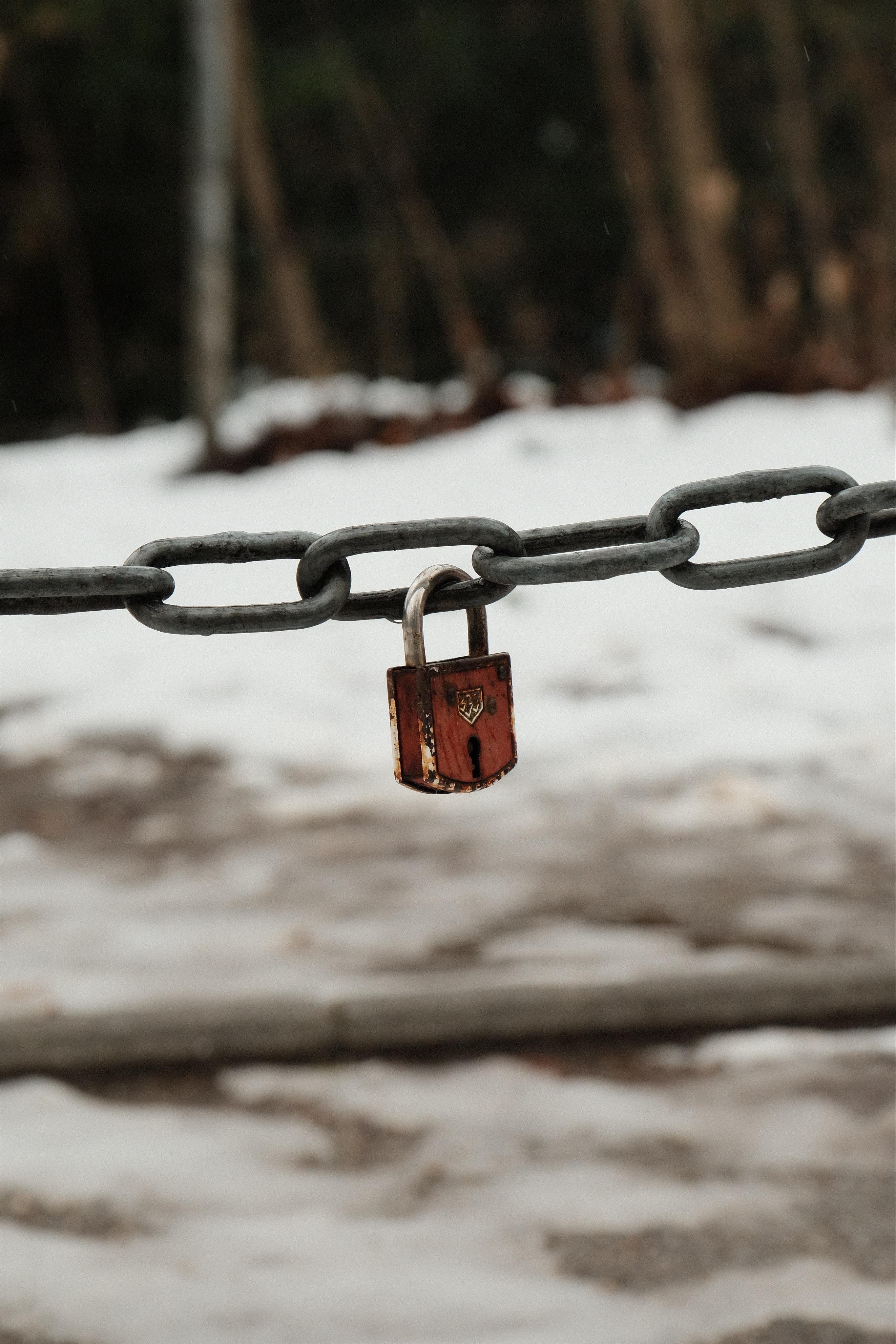 A padlock attached to a chain railing in front of a snowy white background. The red and rusty padlock has a „333“ engraving on the front, which indicates that this might be an antique 1960s ABUS 333 lock.