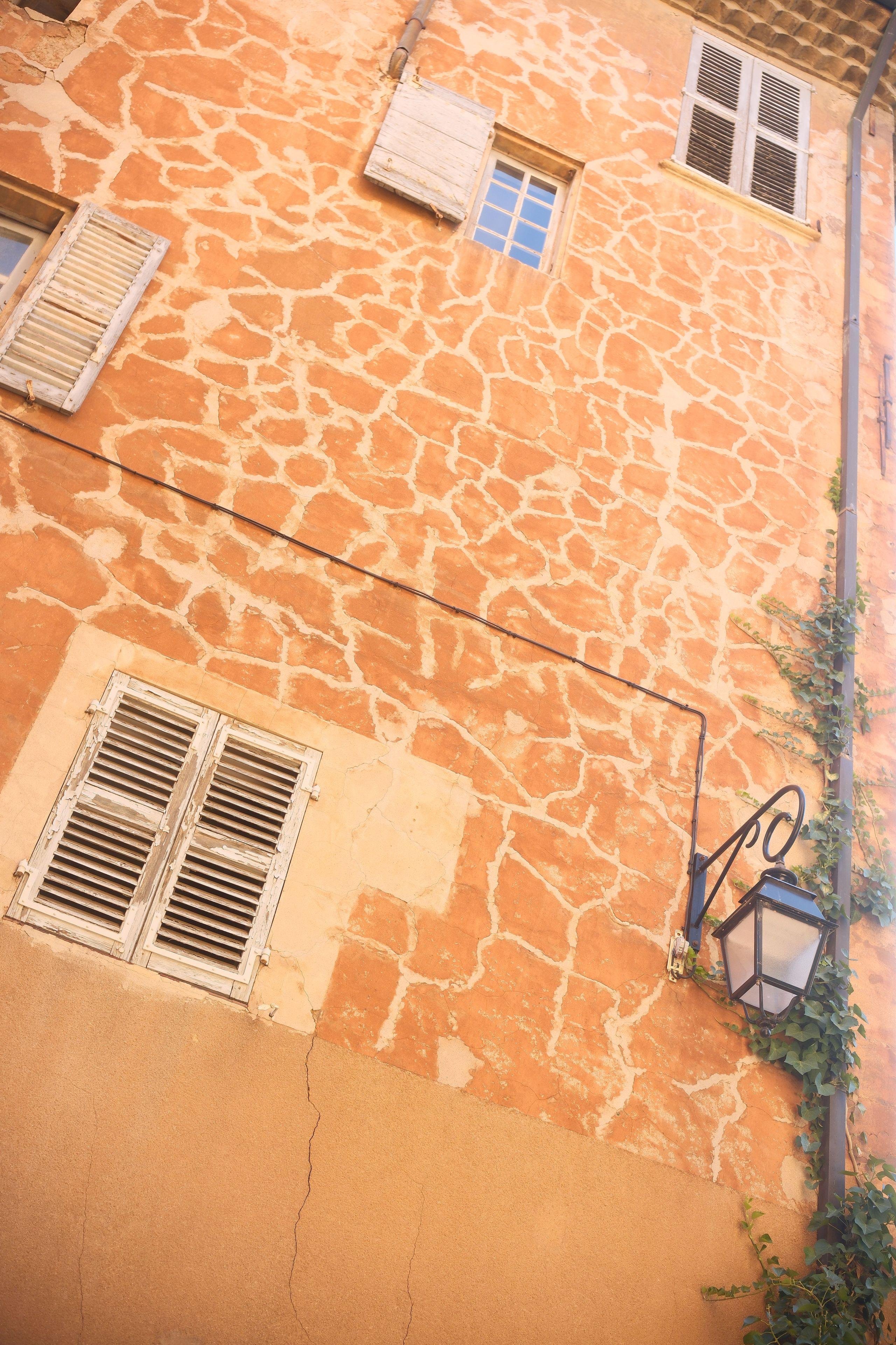 photo format paysage, en contre plongée, d’un mur orange mais avec des traits plus clairs formant ainsi des motifs rappelant la giraffe. Il y a des fenêtres disposées de manière irrégulière