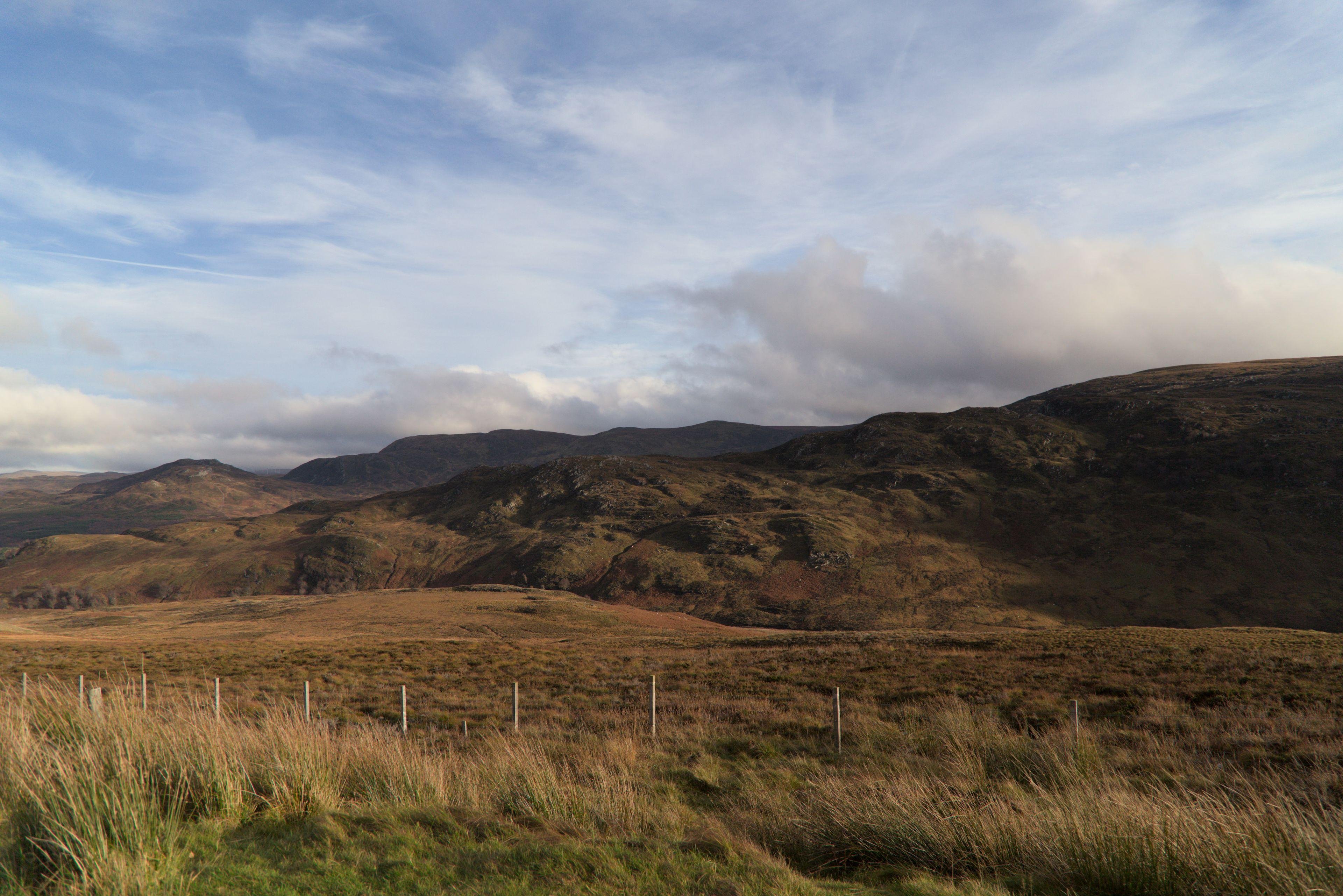 Photo horizontale. Les Highlands Écossais, en teinte de bruns sous un ciel bleu mais très nuageux