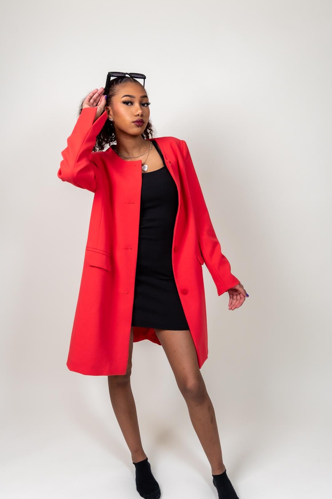 Young woman in a bold red coat and black dress, wearing stylish sunglasses, posing confidently in a photography studio in Lappeenranta.