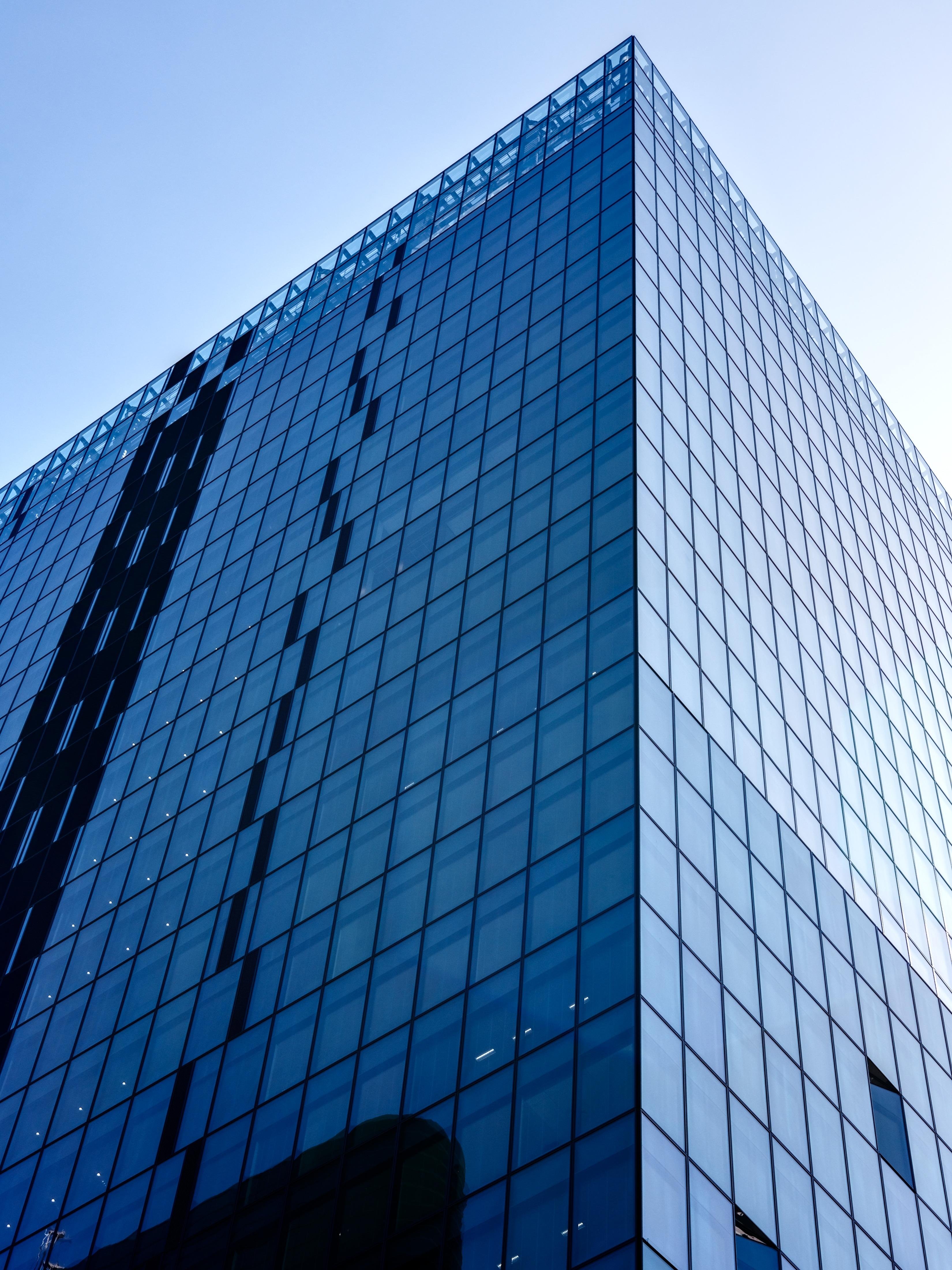 A tall building made of glass and steel. The graphic nature of the picture is emphasized by the simple rectangular shapes and the various shades of blue across the glass surface and the sky.