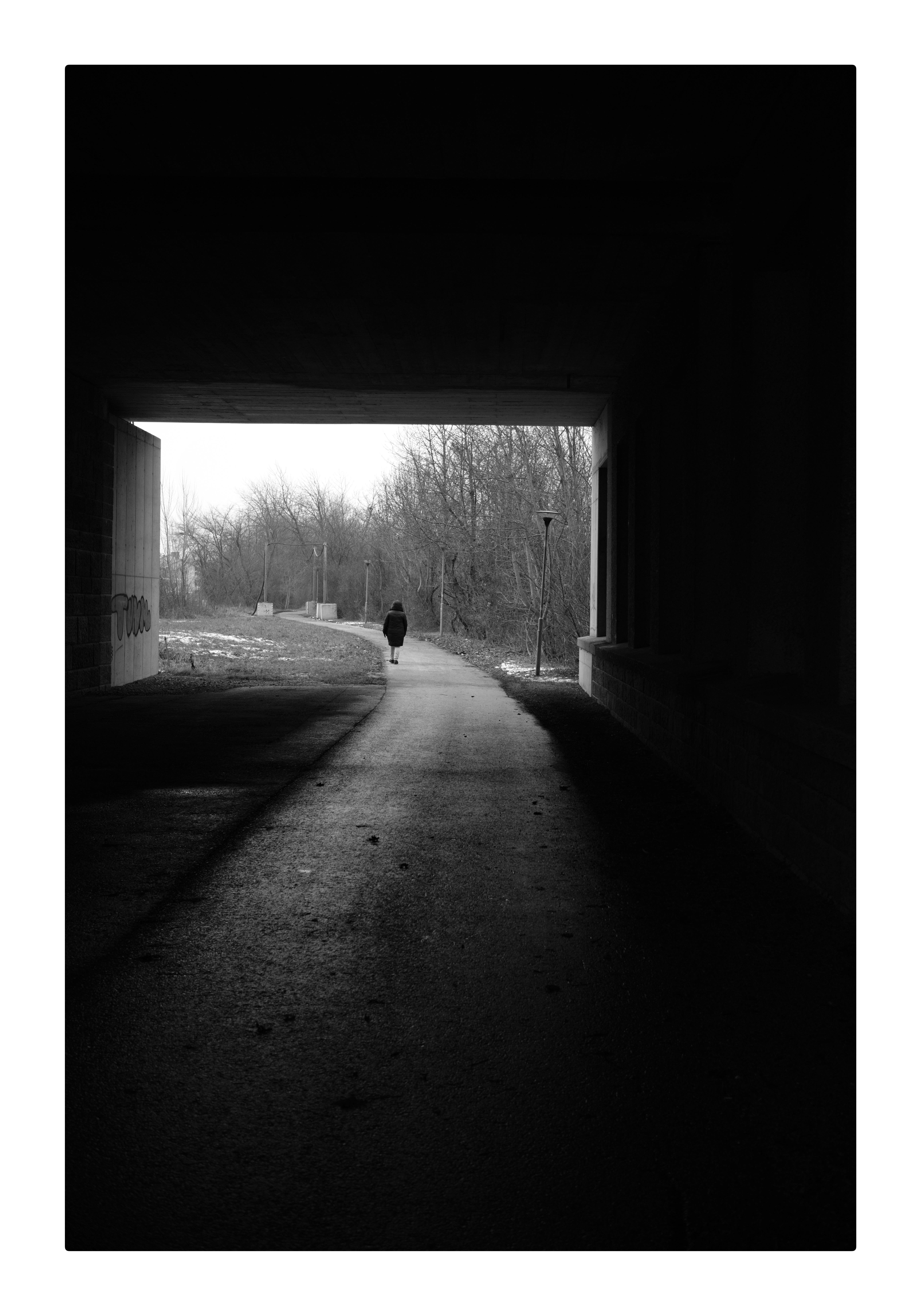 Gehweg unter eine Brücke. Starker Kontrast. Am ende des Weges geht eine Person.