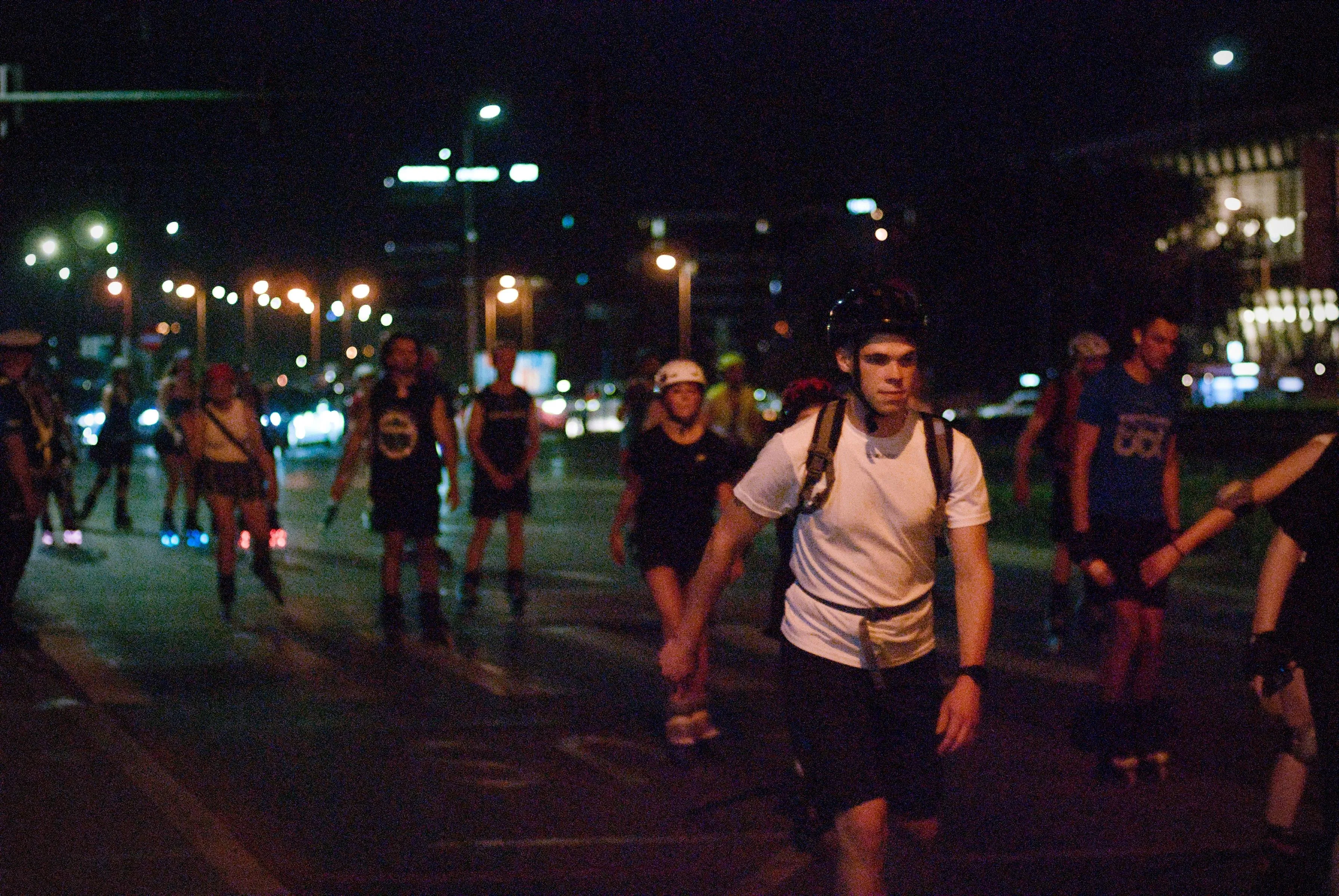 A photo showing bunch of rollerbladers on the street at night