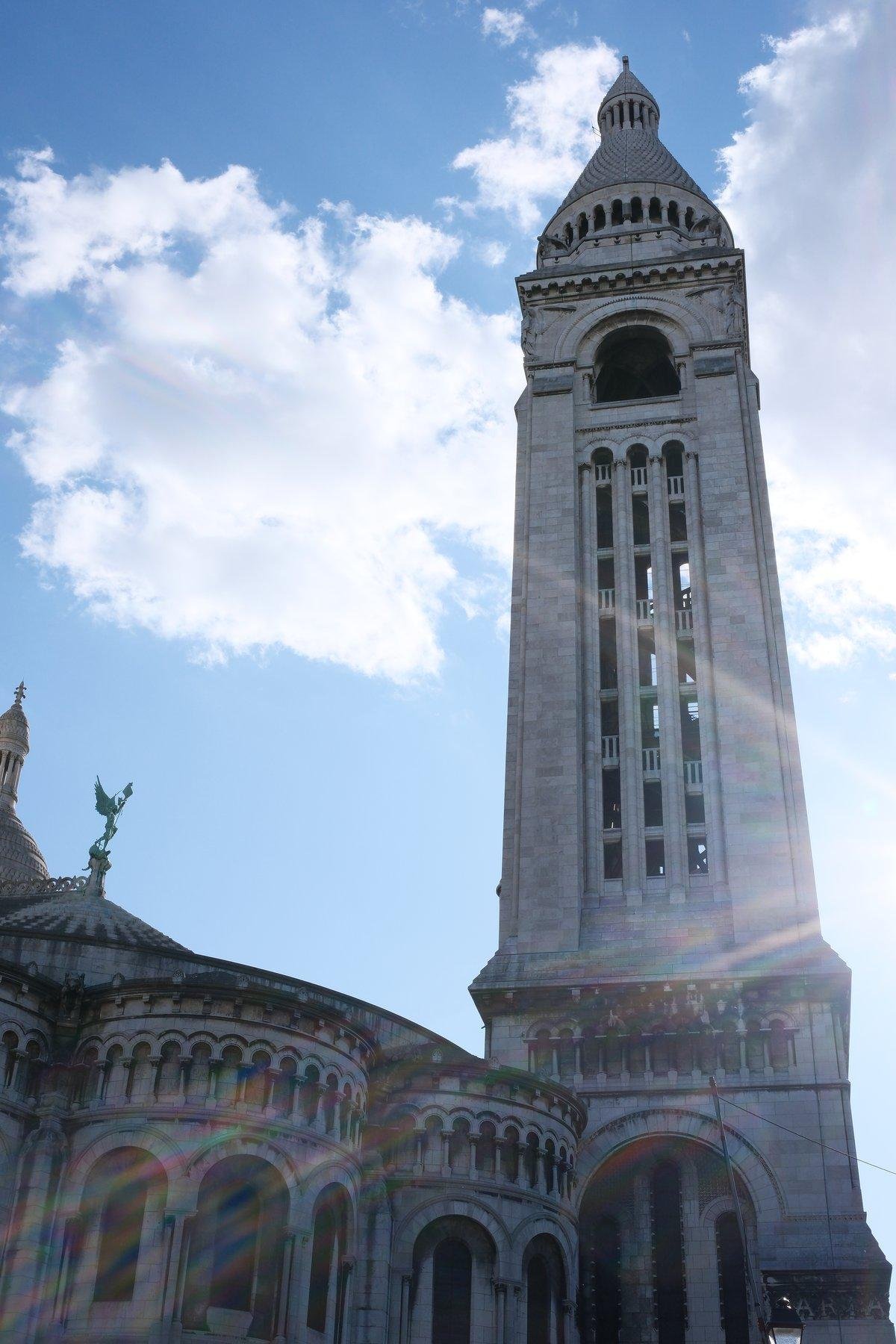 Low angle photo of the bell tower of the Sacrée Cœur in Paris, with a flare of light coming from the right of the pic