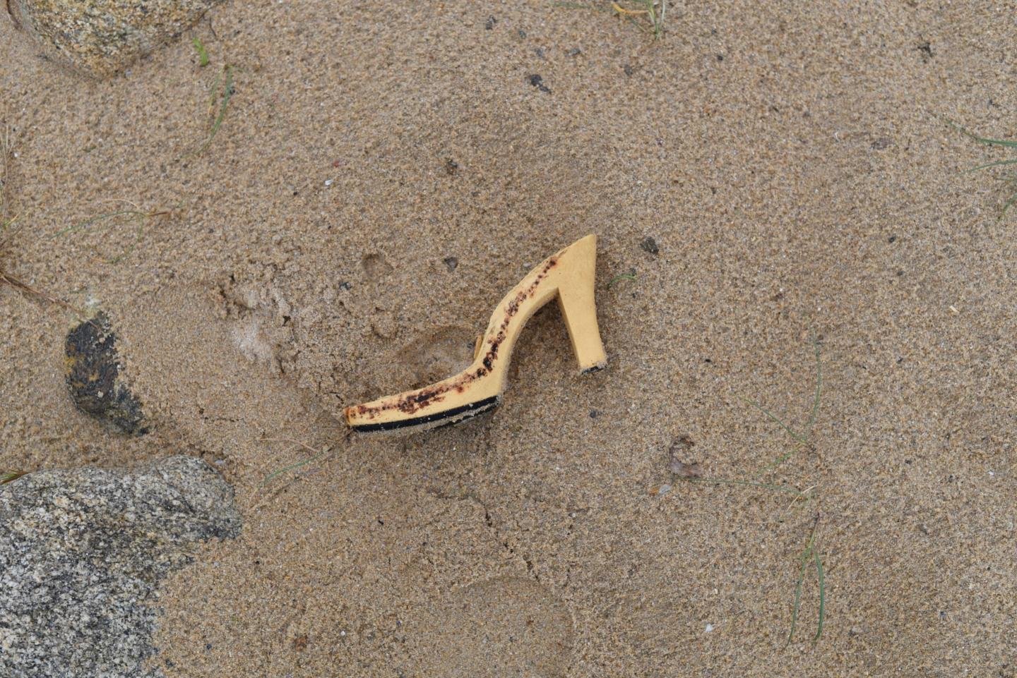 A estructura plástica dun zapato de tacón sobre a area húmeda da praia.