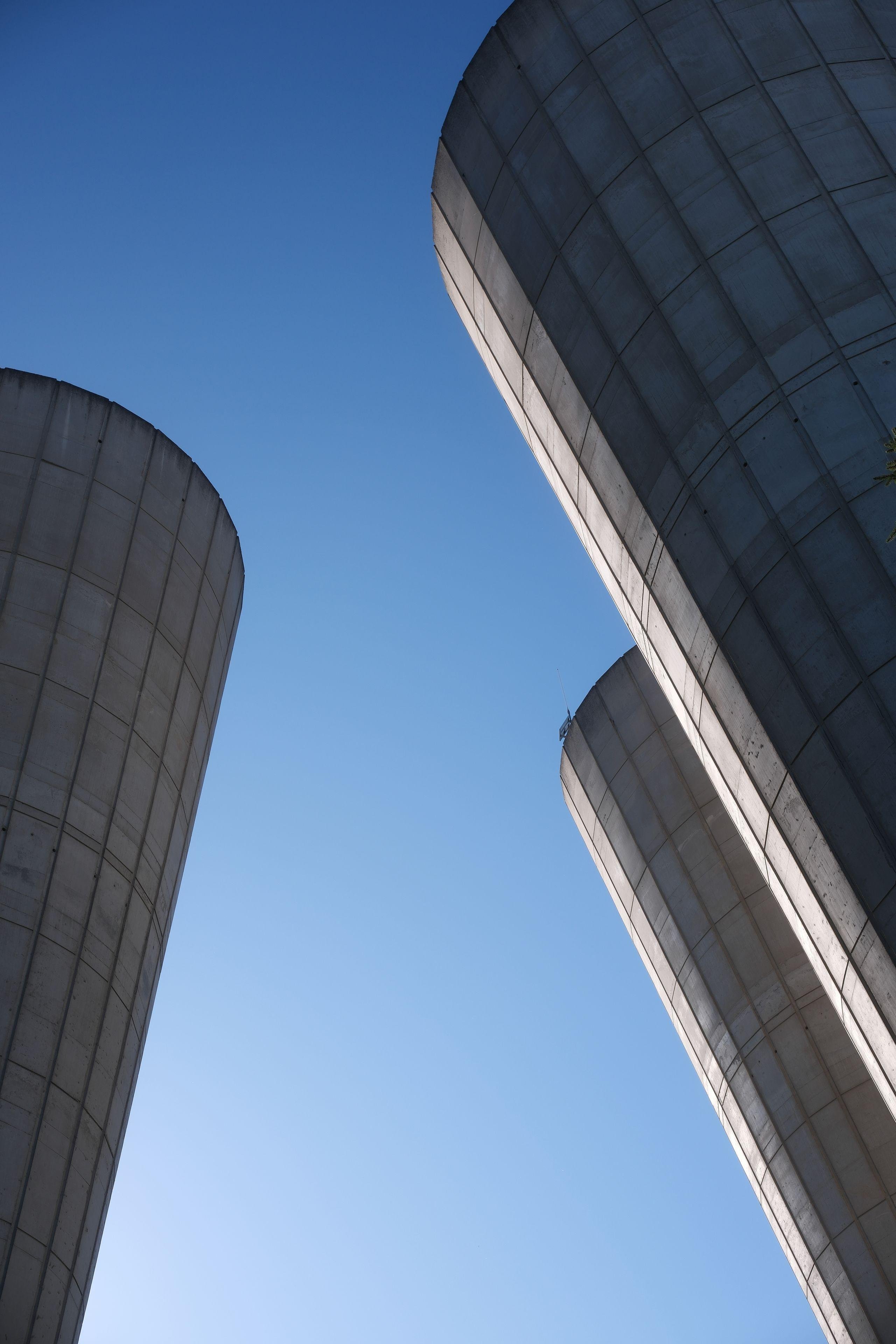 Photo format portrait montrant des morceaux de structure en béton, 1 à gauche, 2 à droite, qui semblent pencher les une vers les autres, sur fond de ciel bleu estival