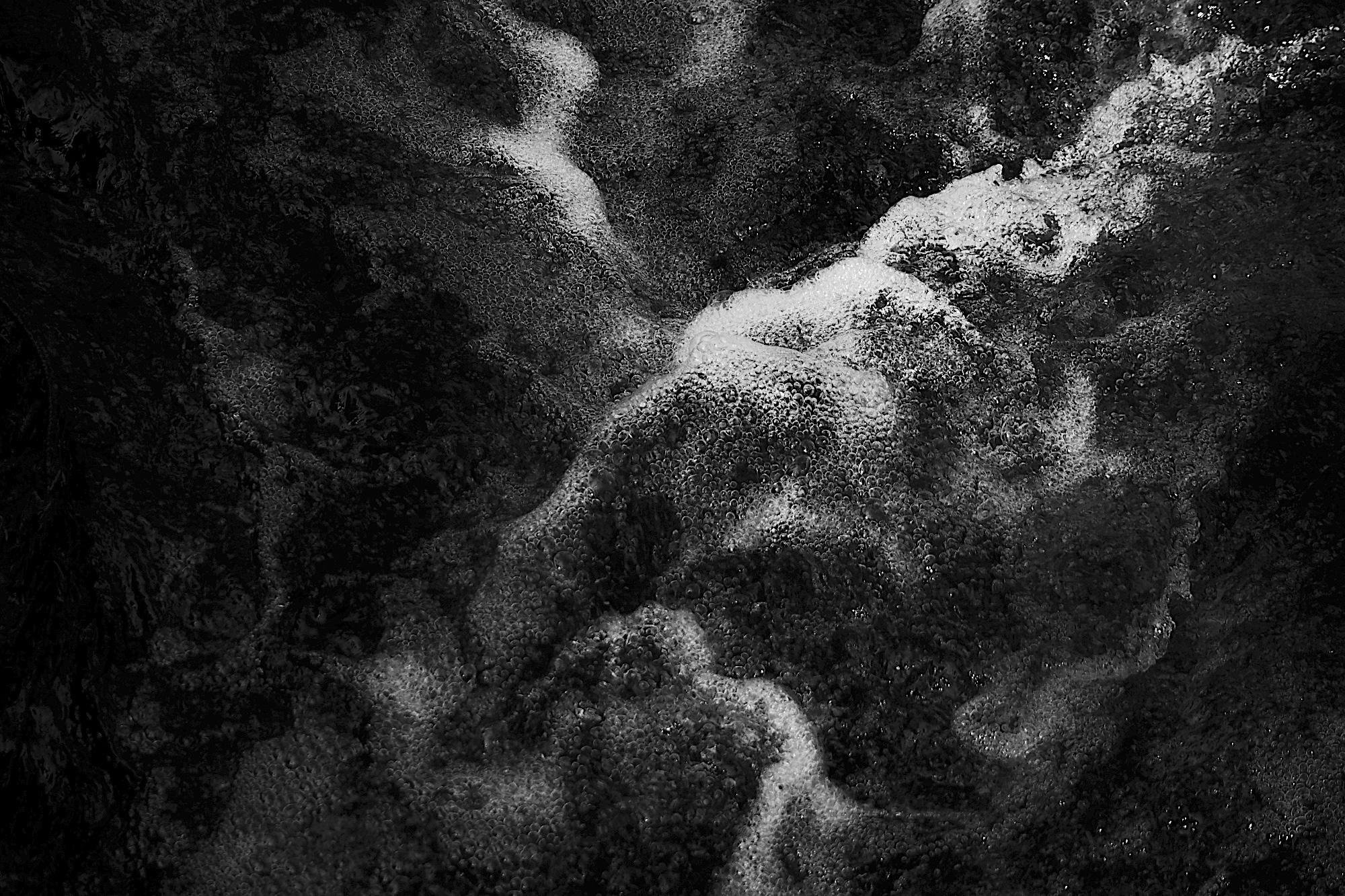 A high-contrast, abstract black-and-white texture featuring swirling water and air bubbles spreading diagonally across the dark background.