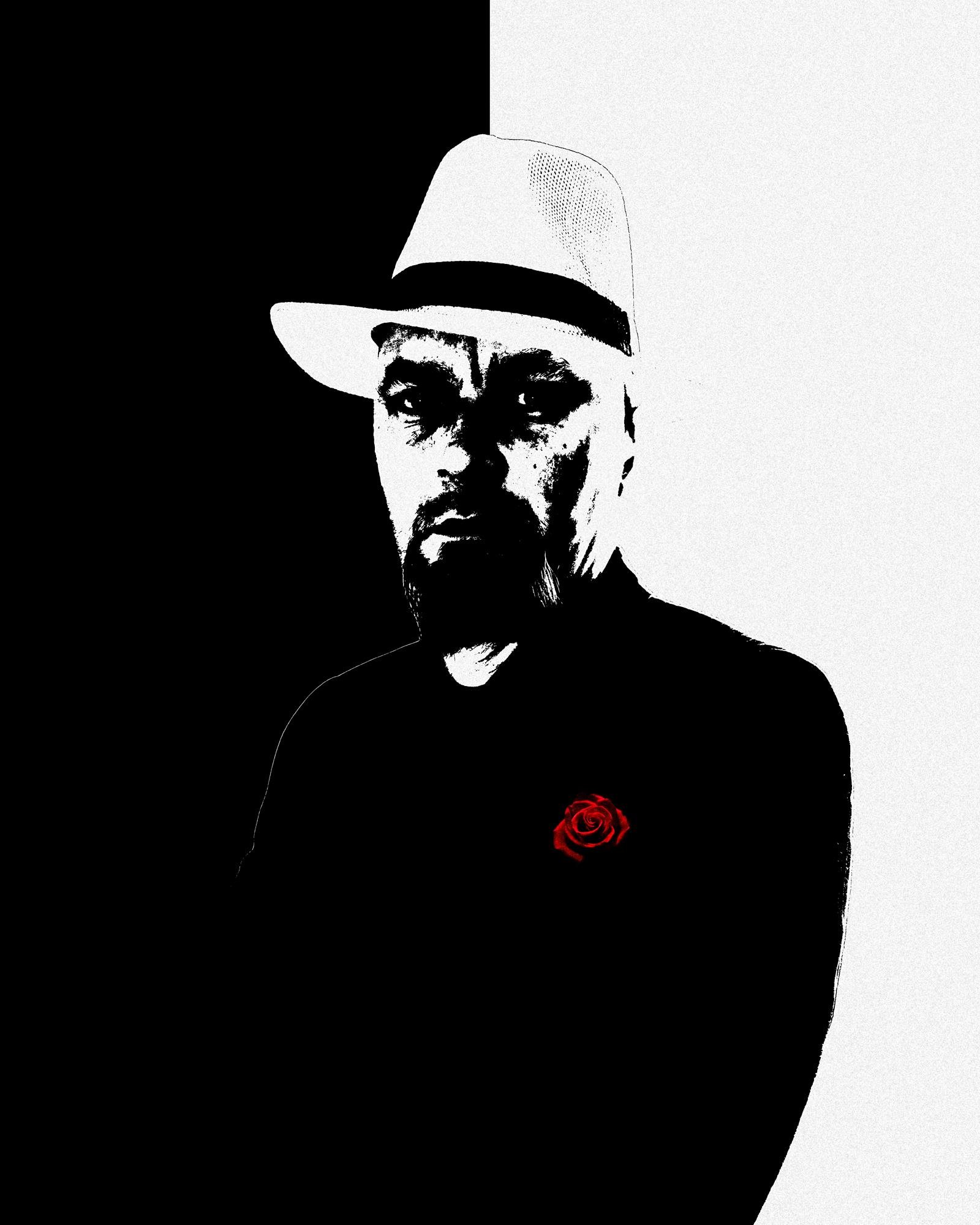 This image is a stylized black and white portrait of a person wearing a hat, with high contrast that highlights the facial features and silhouette. The background is divided into two halves, black on the left and white on the right. The person is wearing a dark outfit with a red rose on the chest.