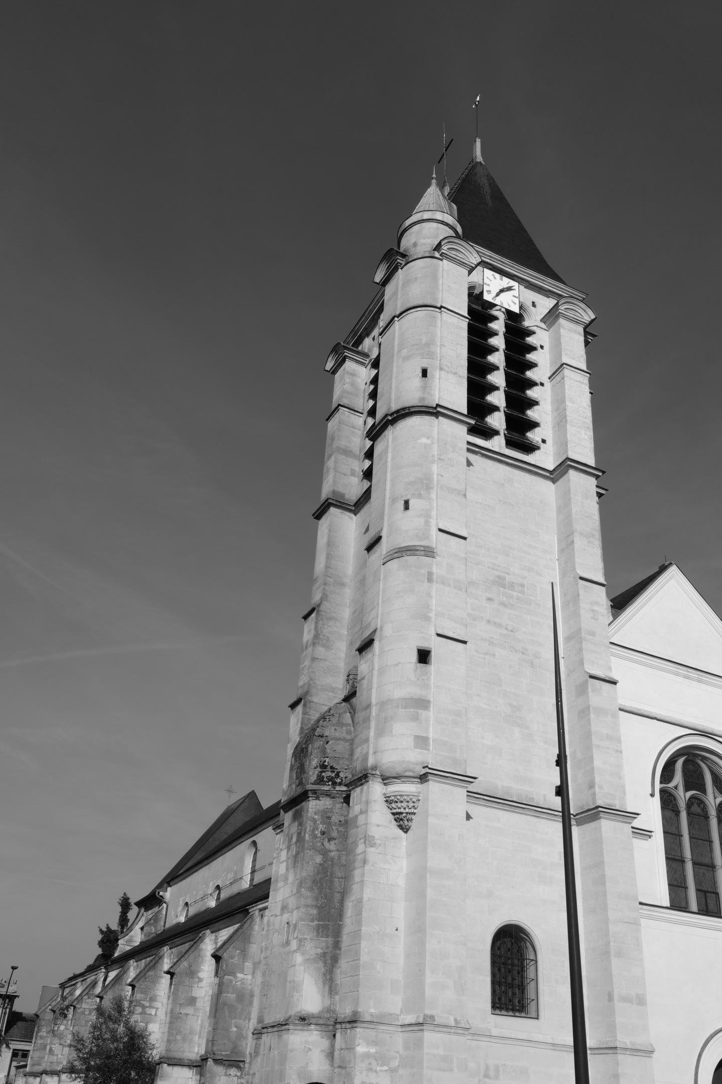 A black and white picture of a church. The attention is on the highest part of the building, the bell tower. A piece of the front is visible on the right and the length of the building on the left of the pic
