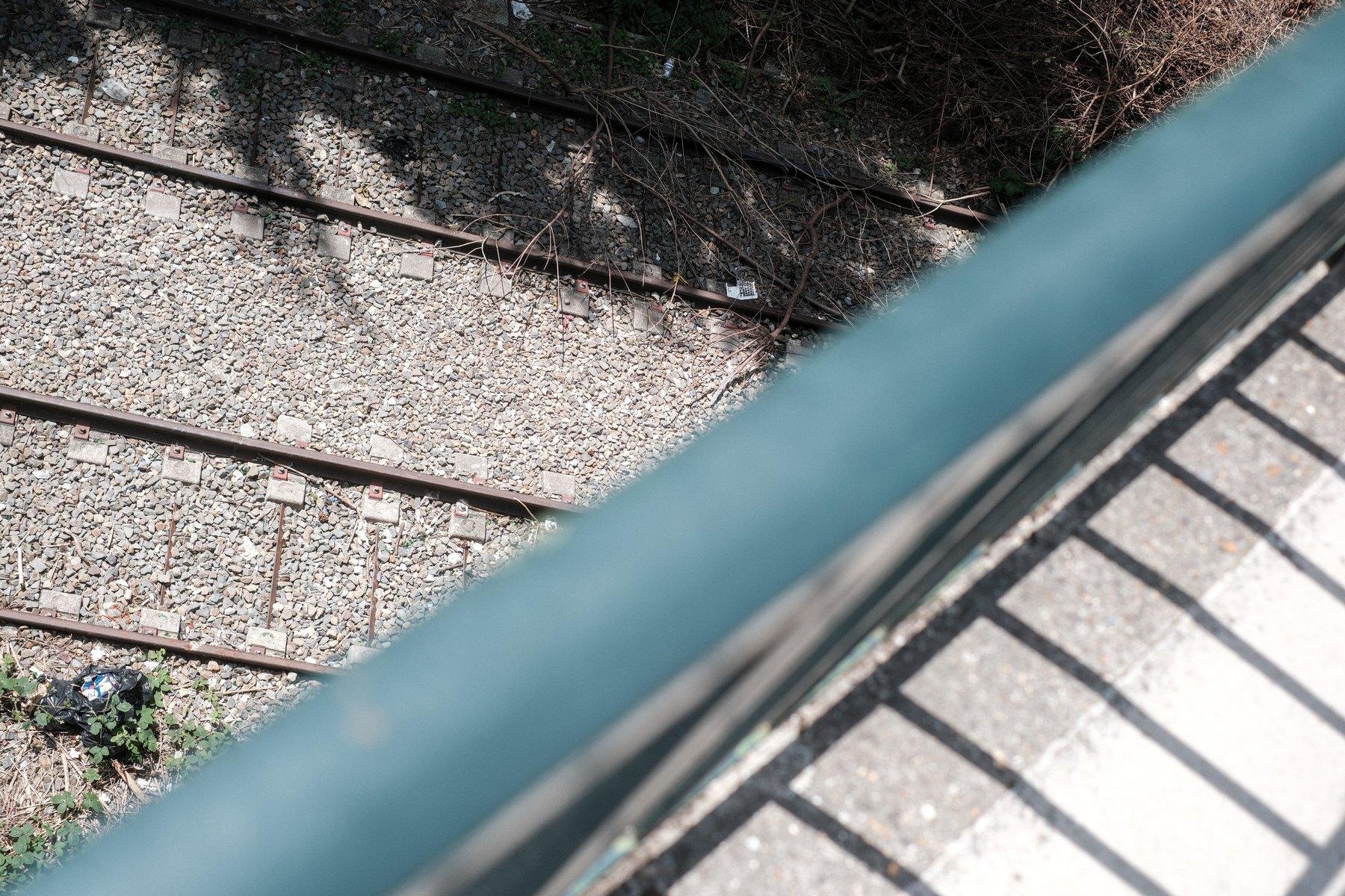 Photo horizontale. Une rampe de sécurité verte viens couper l’image en 2 sur l’axe SW/NE. Au NW, on voit, nette, 2 voies ferrées et leur cailloux, au SE, flou, du bitume du pont sur lequel je me tiens