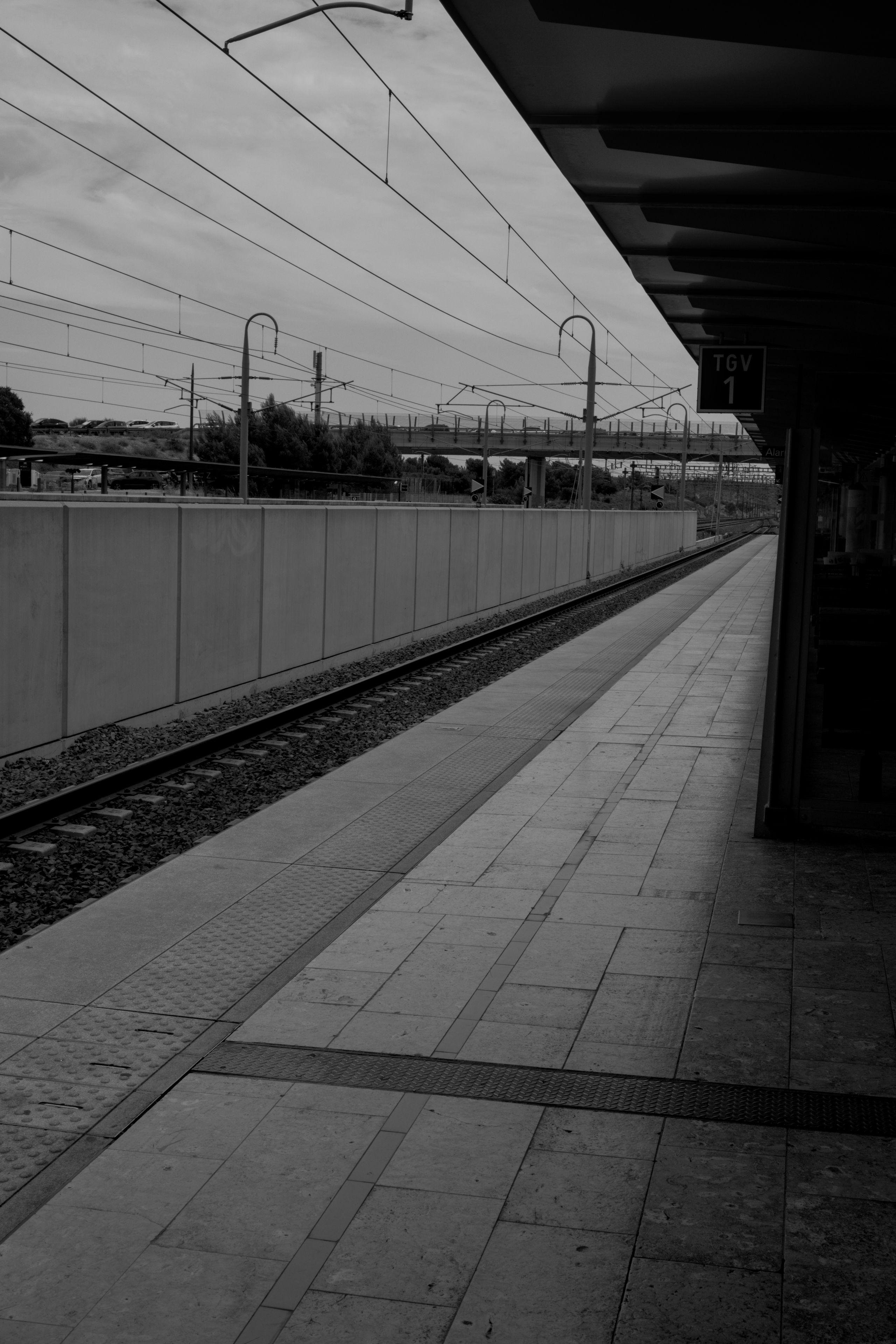 Photo verticale en noir et blanc. Un quai de gare, vide.