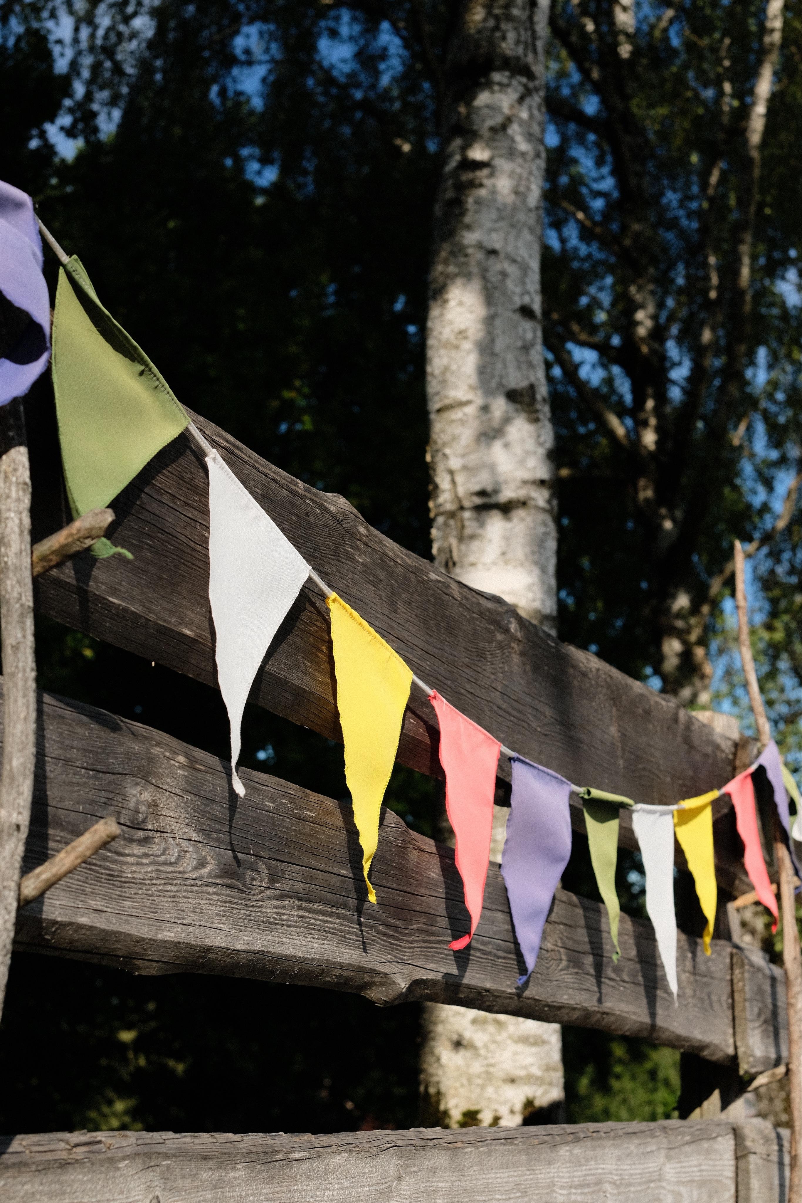 A colourful pennant chain appended to a wooden fence. In the background a birch tree.