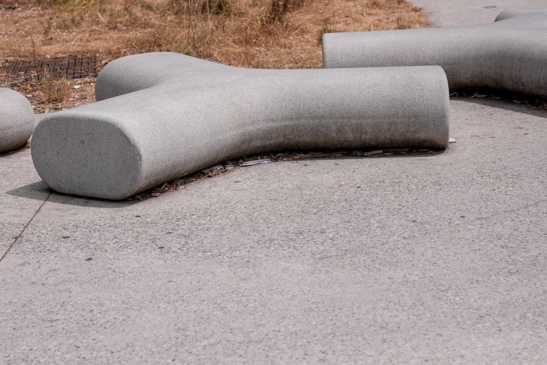 Photo horizontale. Une structure en béton à 3 branches aux angles arrondis, servant de mobilier urbain, des bancs