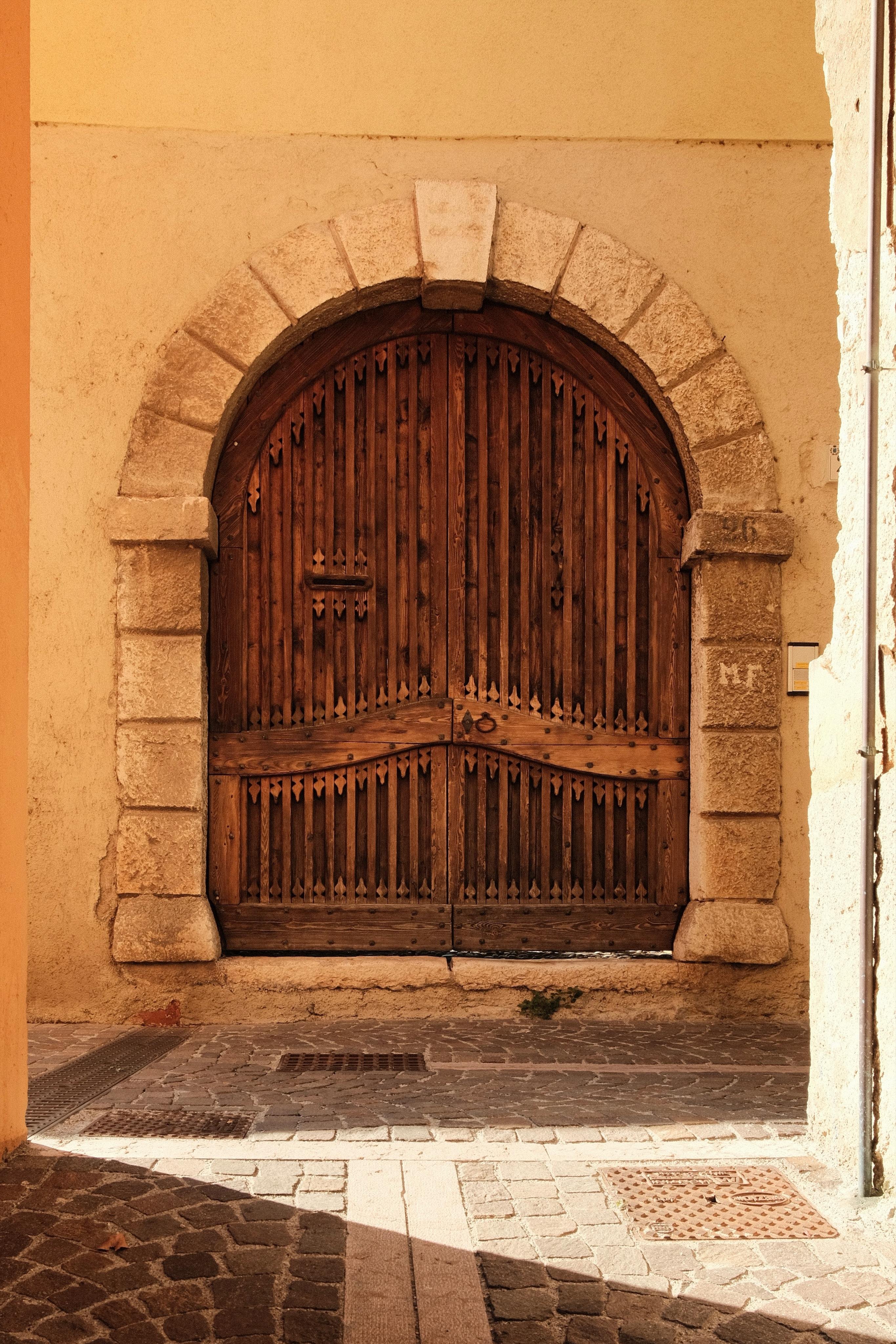 A large, ancient-looking wooden door with an arches top, framed by an arch of large stones set in a yellow-orange wall.