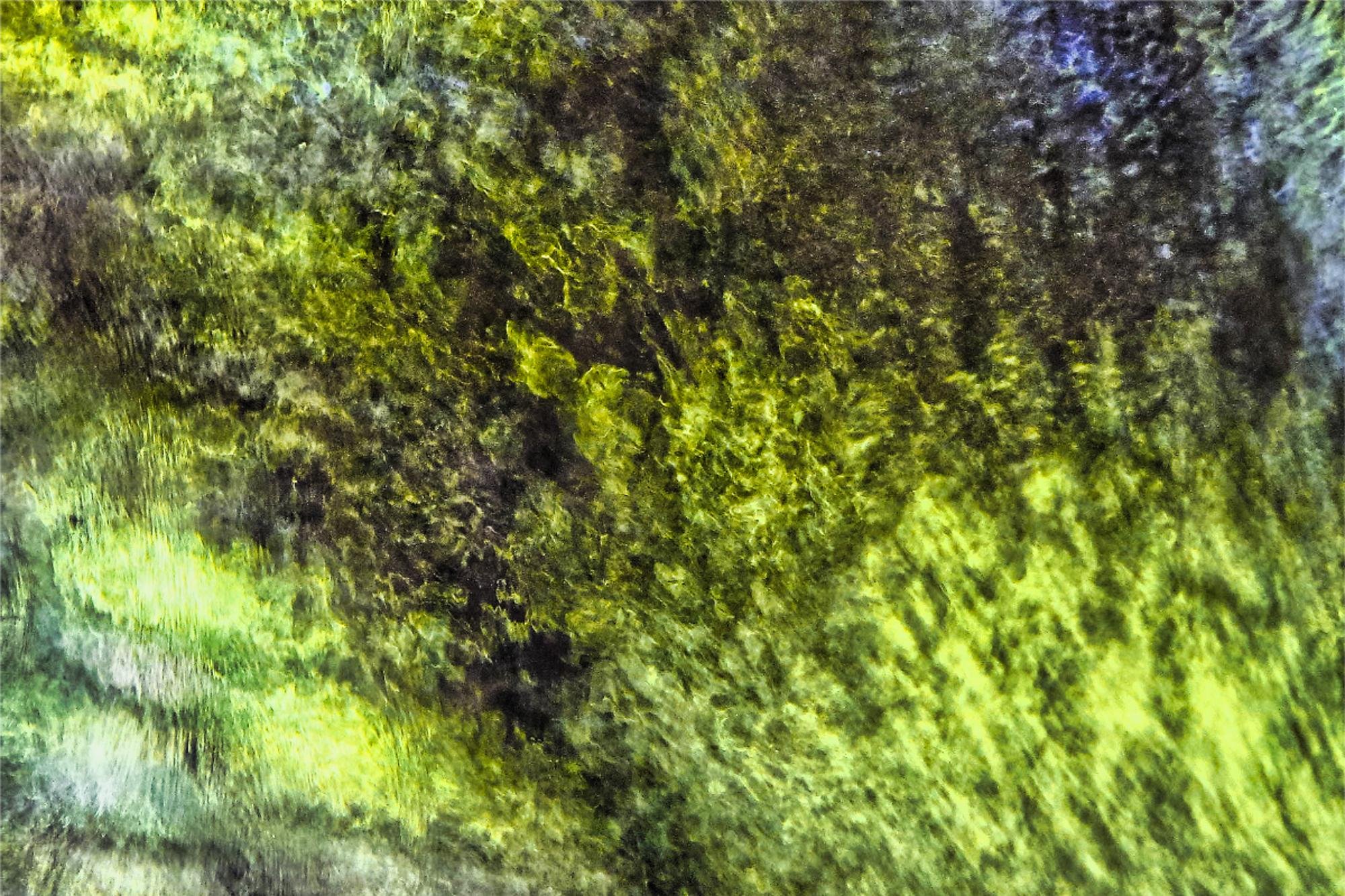 An abstract texture blurred by movement, featuring mottled shades of green, yellow, and dark gray, with diagonal stripes. It depicts the rapid movement of water on the surface of a stream, reflecting the foliage of trees.