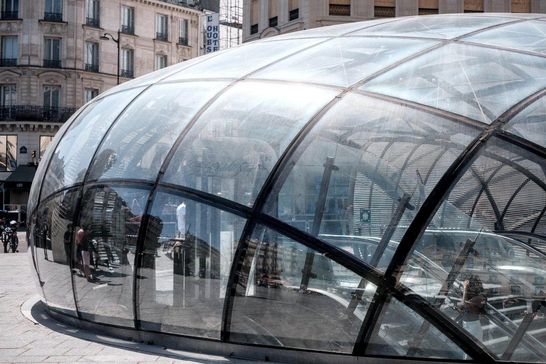 Photo horizontale. Une entrée/sortie de métro en forme de bulle en verre aplatie