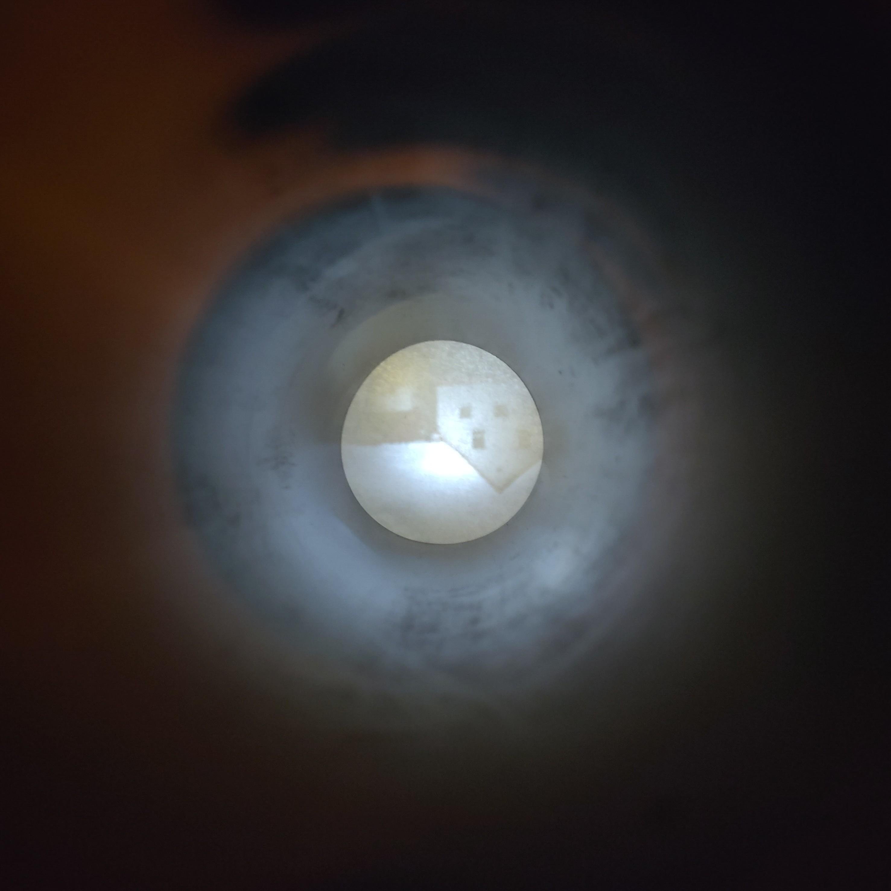Foto im Querformat, fotografiert in eine Röhre hinein.
In der Bildmitte befindet ein rundes, auf dem Kopf stehendes Abbild eines Einfamilienhauses.
Darum verläuft ein Ring, in dem die Röhrenwand beschienen wird.