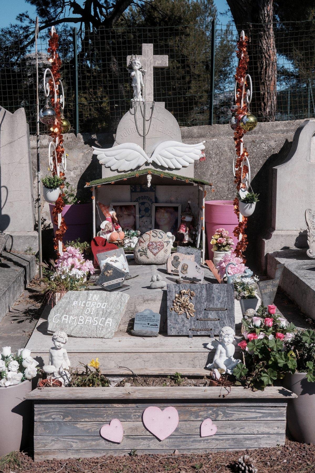 Photo verticale. Une tombe décorée de manière inhabituelle : des guirlandes, des boules de sapin, une jardinière avec des cœur en façade, une crèche abritant des photos de la défuntes et une affiche de fan de l’OM en j’en passe