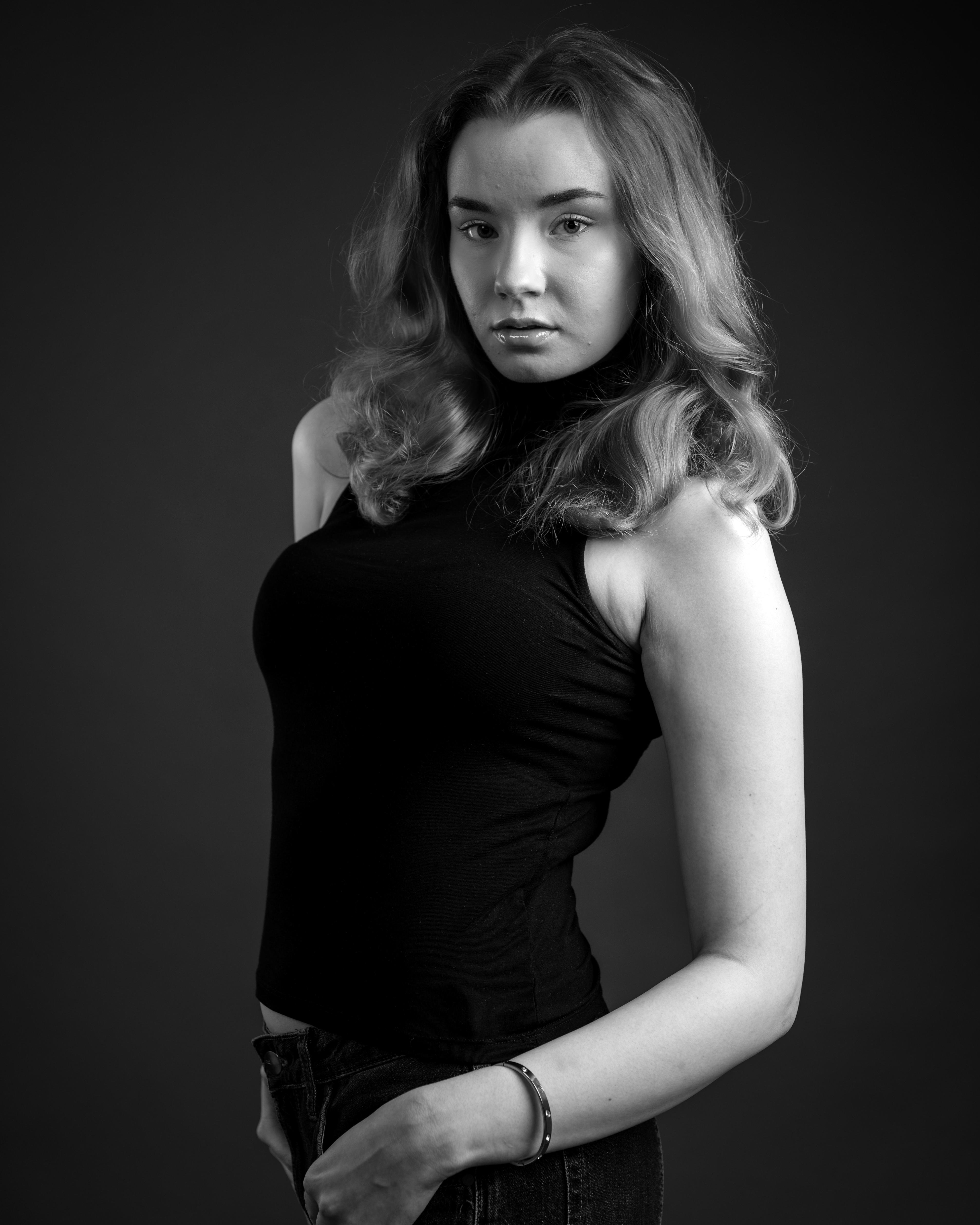 This is a black and white portrait of a person. They have long hair and are wearing a sleeveless top. The image has a dramatic and artistic feel due to the lighting and pose. Valokuvaaja Kuvaajankulma Lappeenranta