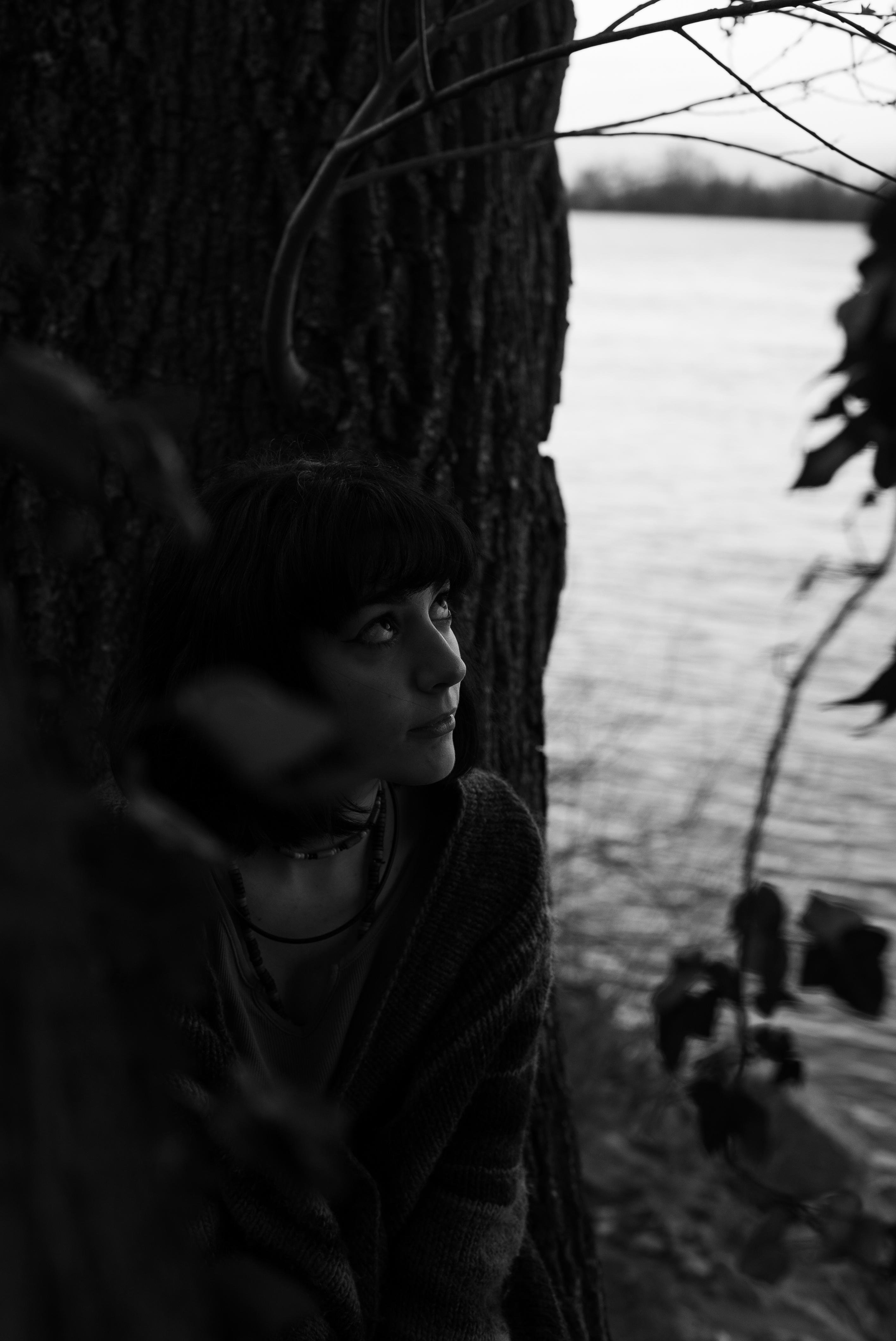 a girl watching upward near a tree and a river