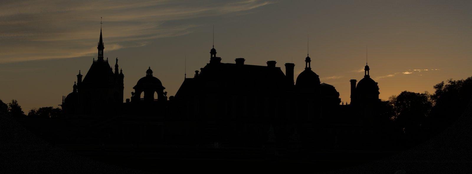 Photo paysage de la silhouette en contre jour du château de Chantilly, sur fond de ciel du crépuscule et ses teintes orangées