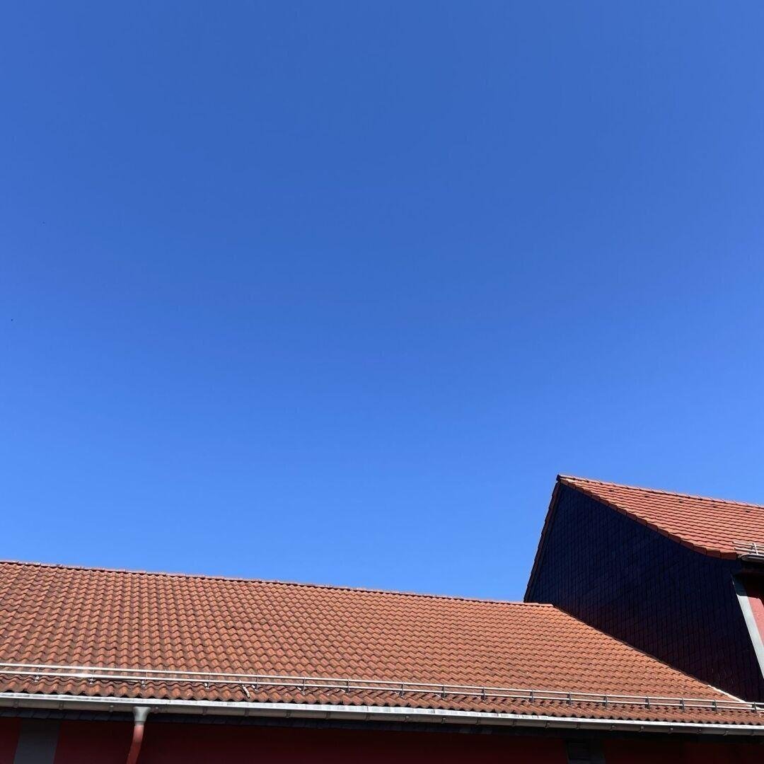 Strahlend blauer Himmel. Im Vordergrund sieht man ein Dach mit roten Ziegeln.