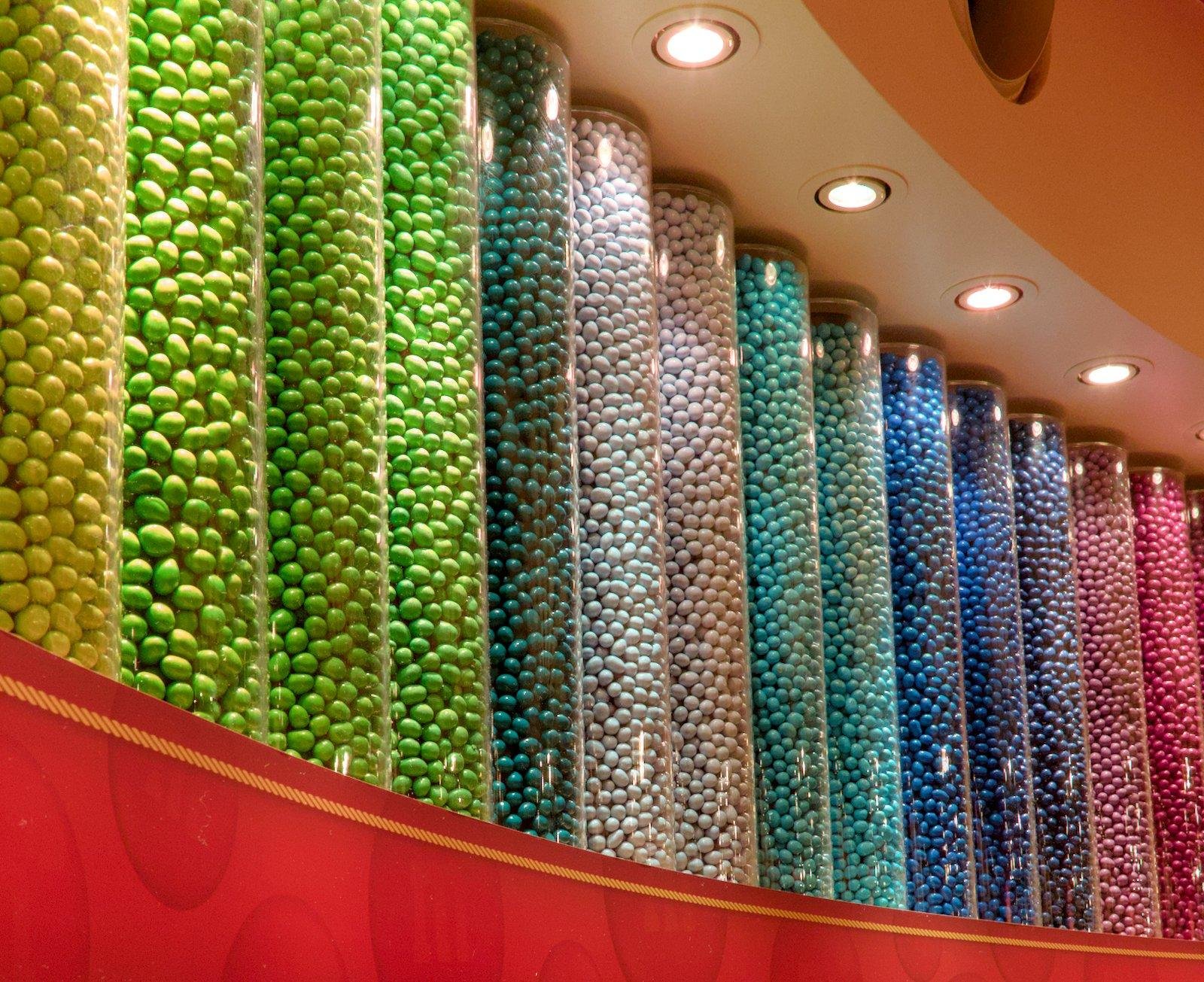 Un mur avec de gros tubes transparent, chacun remplis de M&Ms d’une même couleur, formant un dégradé de couleurs