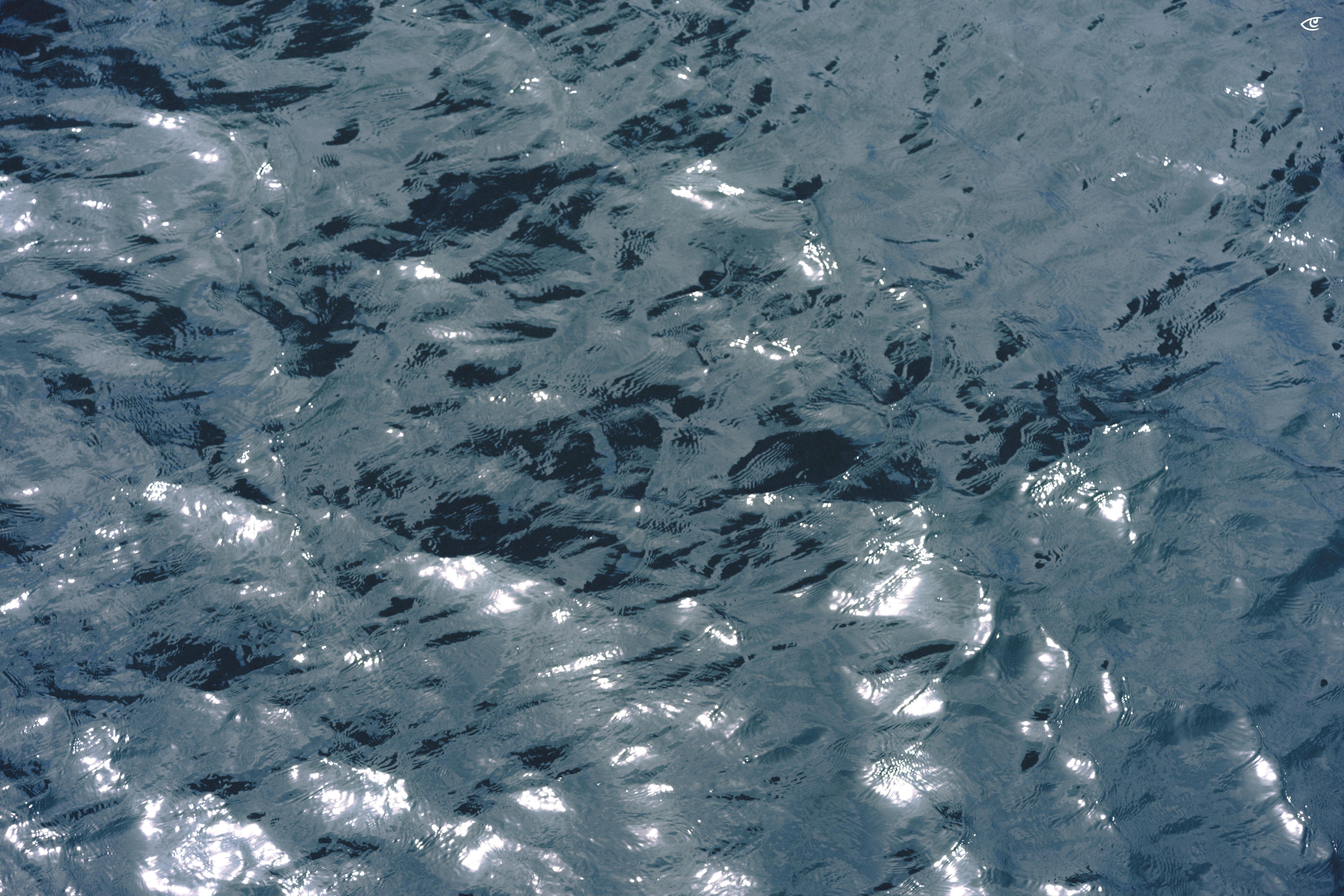 Close-up of rippling blue-gray water with small waves and bright sunlight reflections scattered across the surface.
